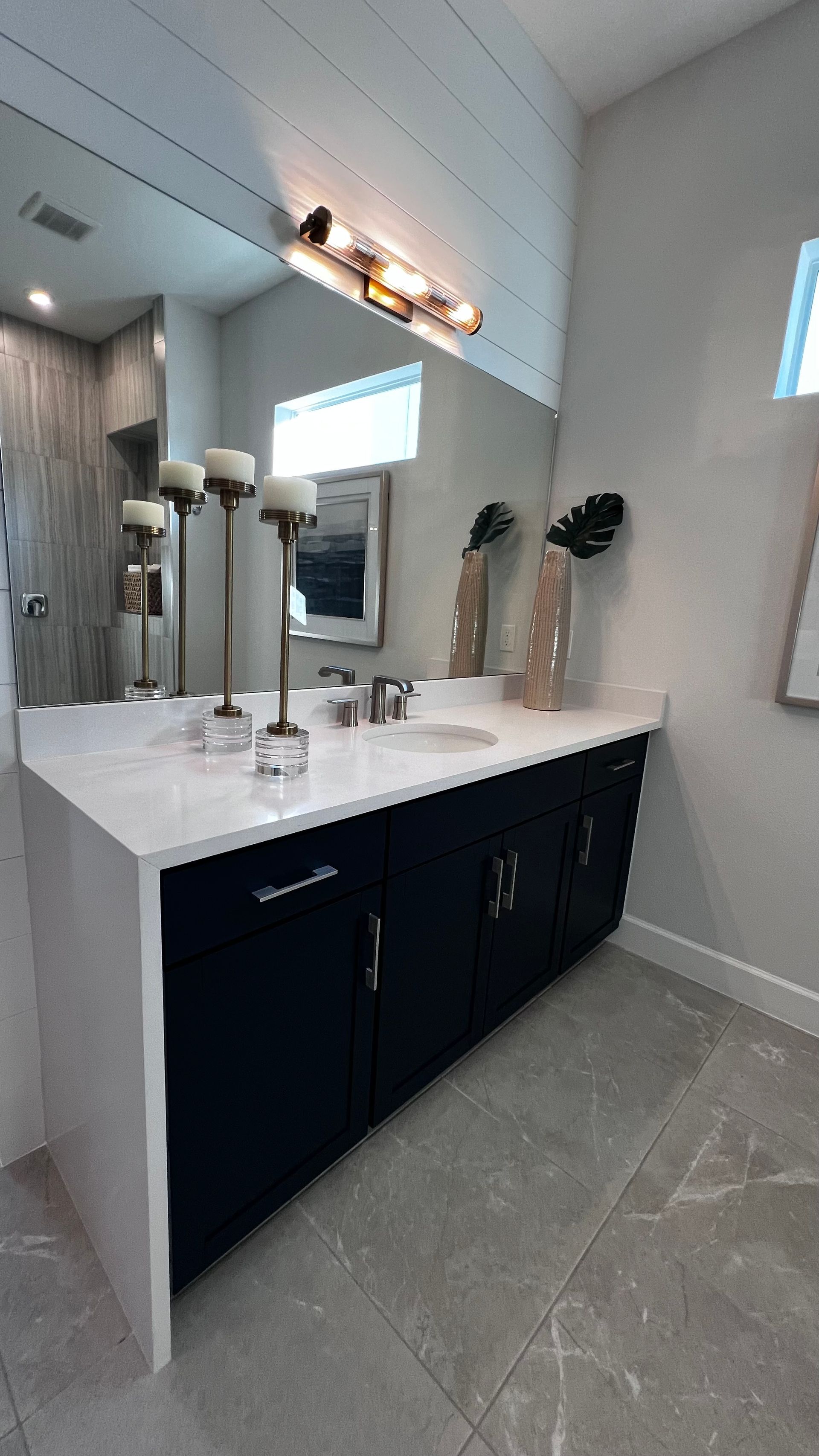 Modern bathroom vanity with a white countertop, large mirror, and navy blue cabinets on gray tiled flooring.