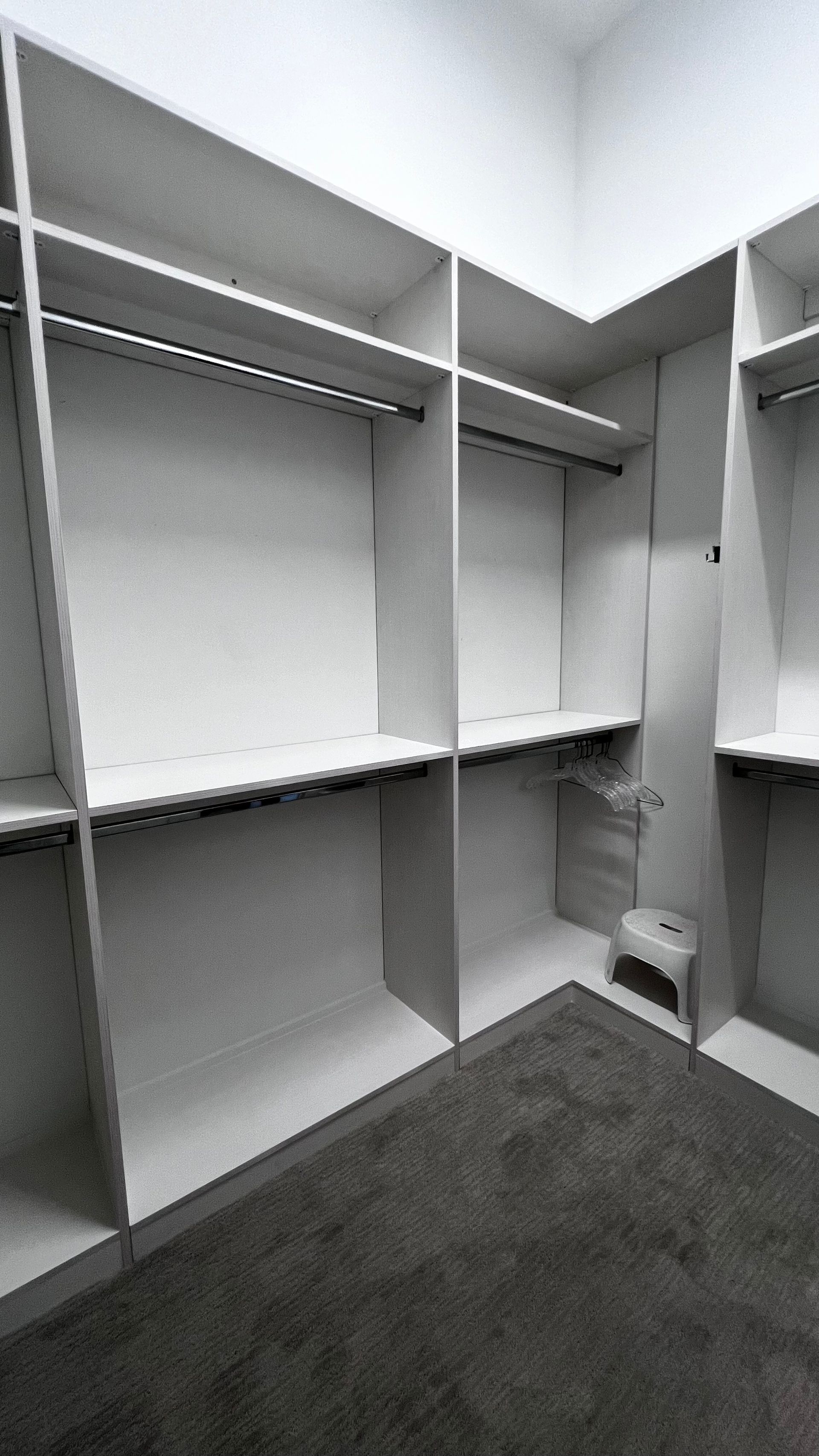 A walk-in closet with white shelving, hanging rods, and dark gray carpeting.