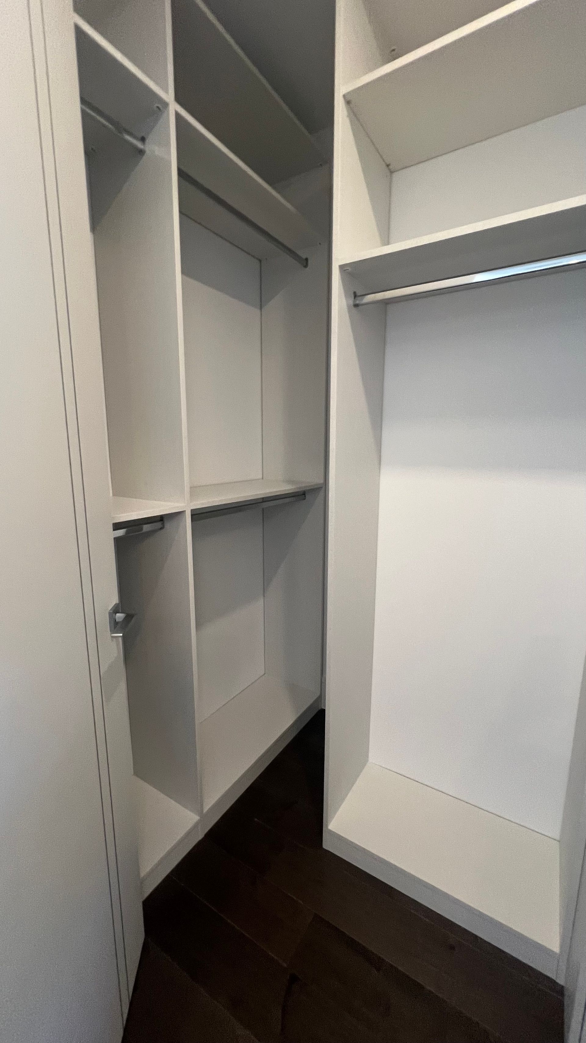 Empty walk-in closet featuring white shelves, hanging rods, and dark wooden floors.
