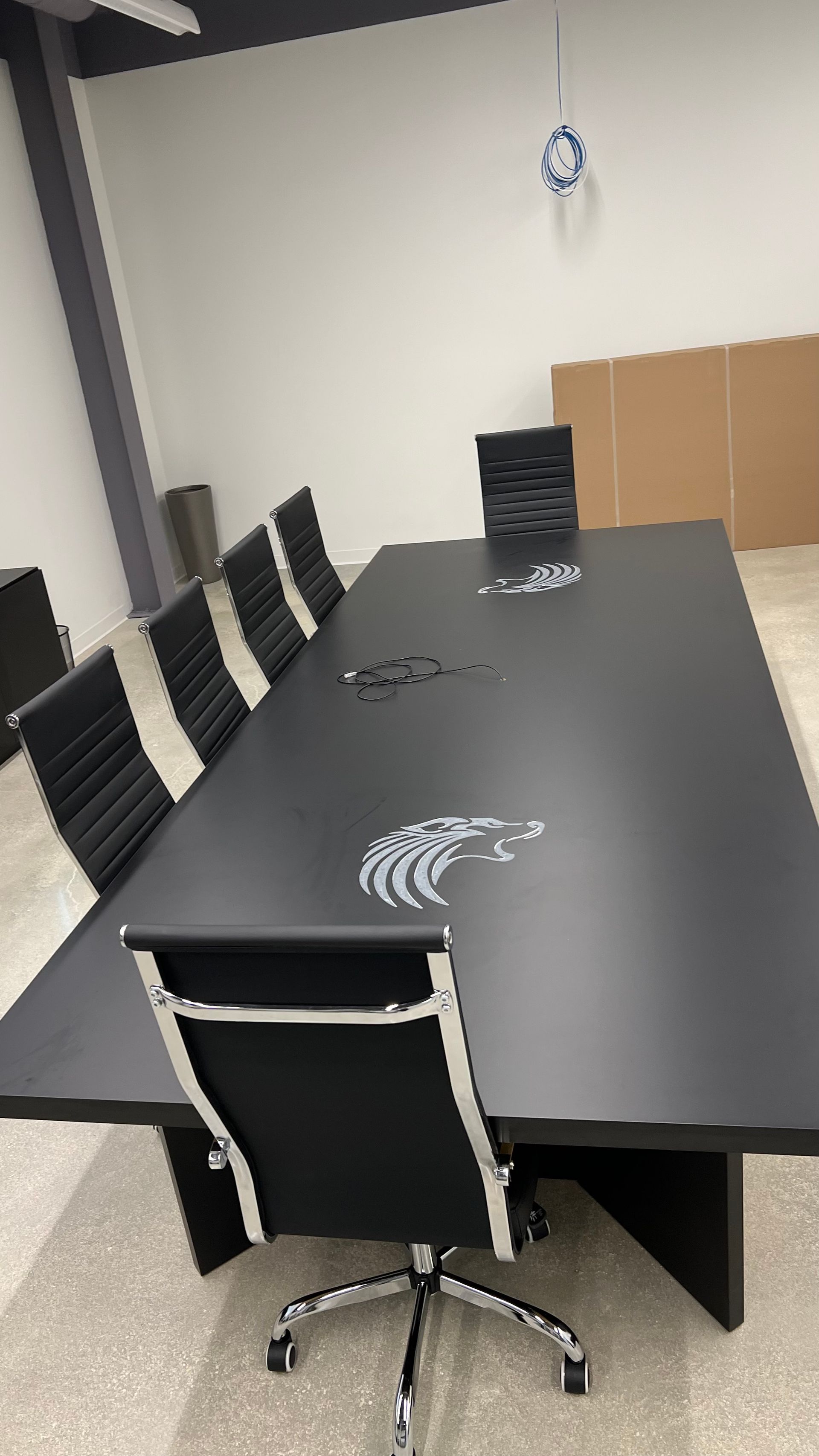 A long black conference table with several black chairs in a modern, sparsely furnished office space.