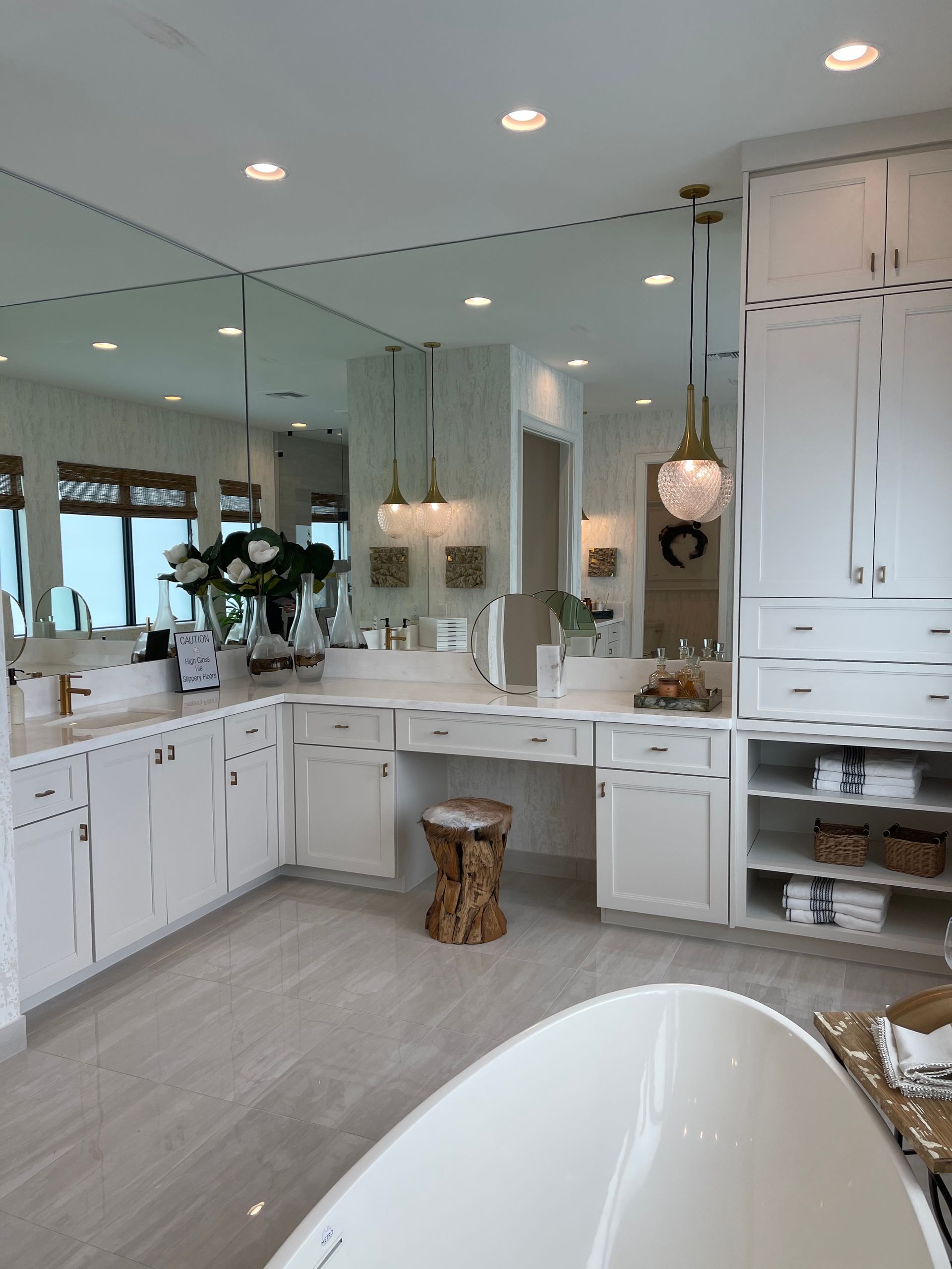 A white, modern bathroom features a large vanity, mirror, walk-in closet shelving, and a standalone tub in the foreground.