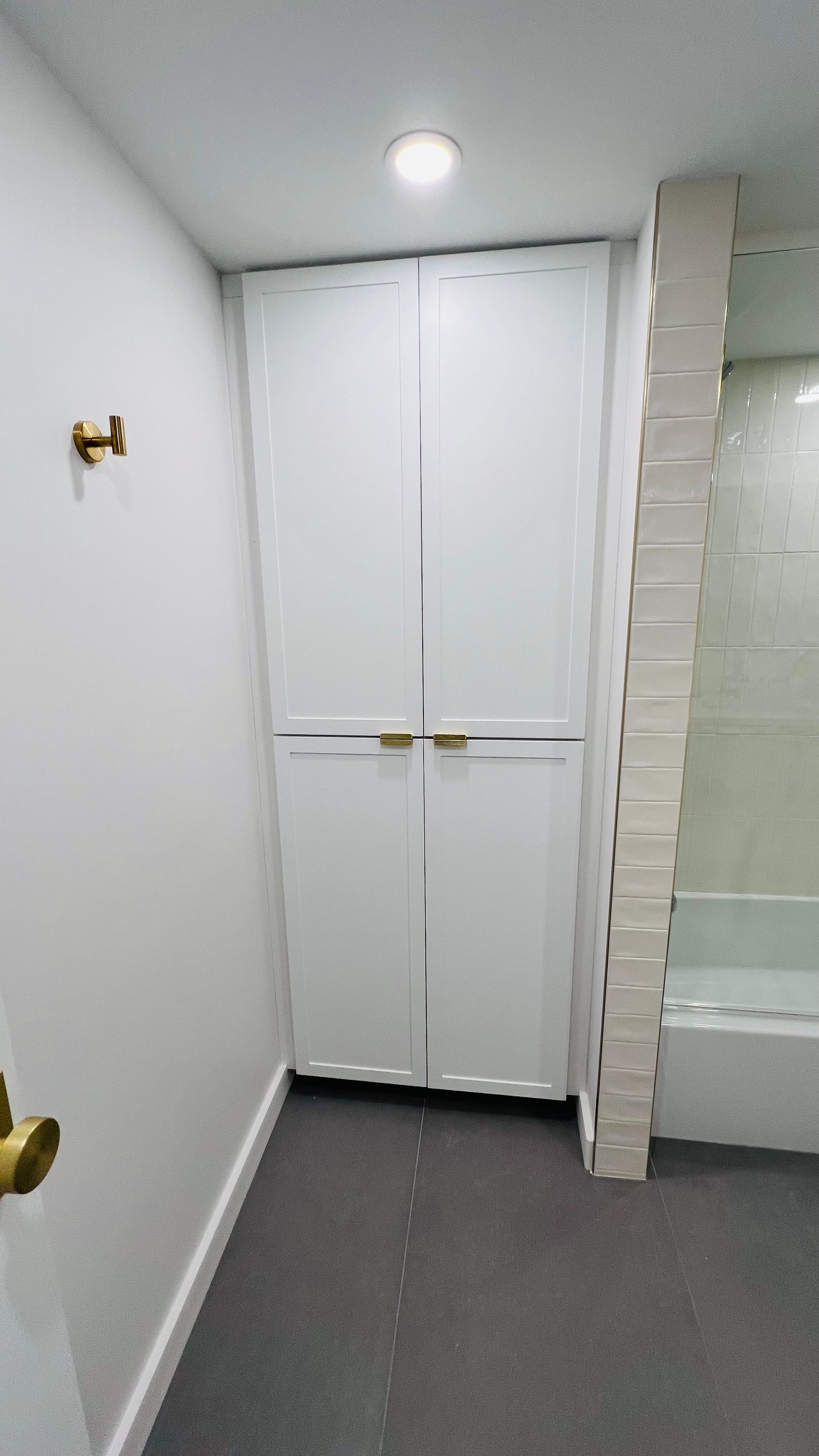 White full-height double cabinets in a room with grey carpet, adjacent to a tiled bathtub area.