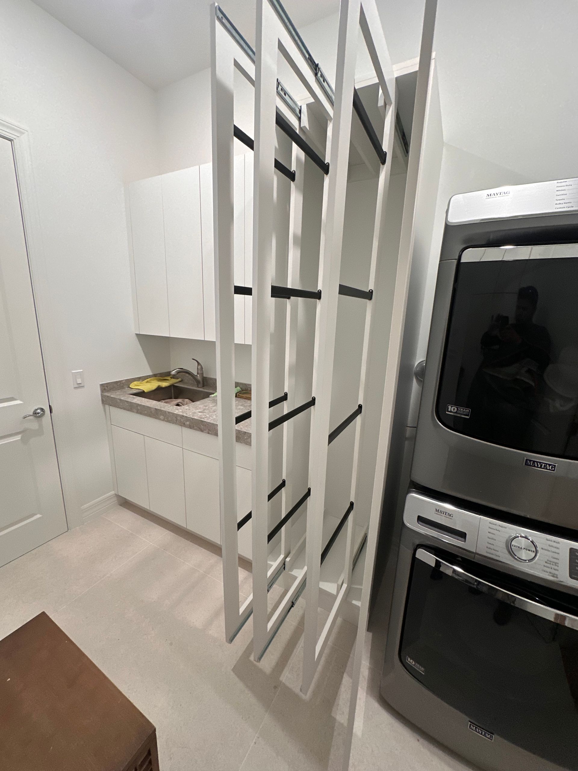 A white pull-out pantry organizer unit in a laundry room next to a stacked washer and dryer.
