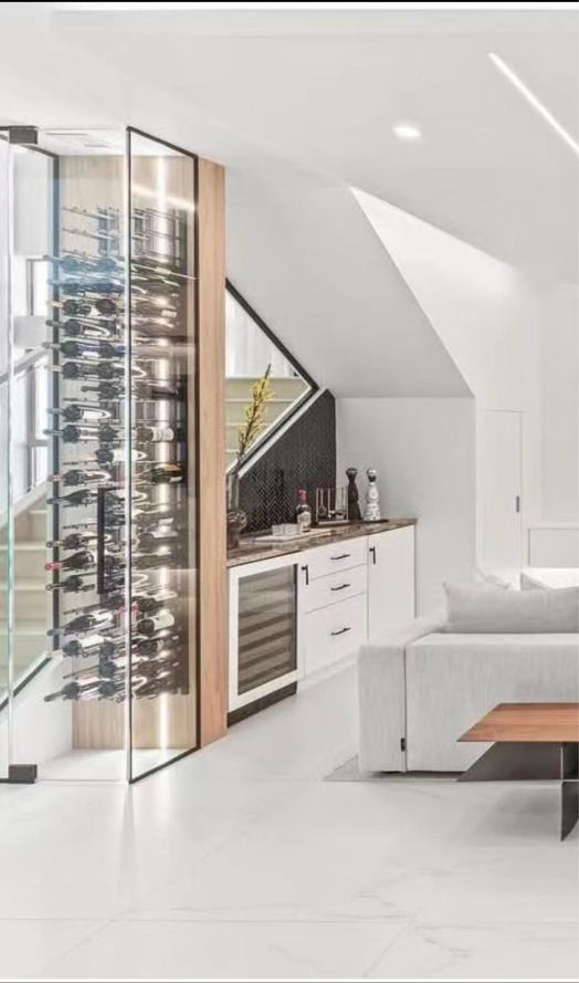 A modern home bar featuring a floor-to-ceiling glass wine cabinet next to white cabinetry and a seating area.