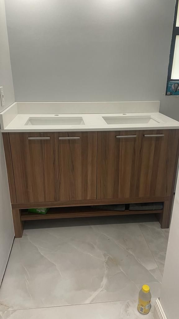 A modern, wood-grain double vanity with a white countertop and rectangular sinks, situated in a bathroom with tiled floors.