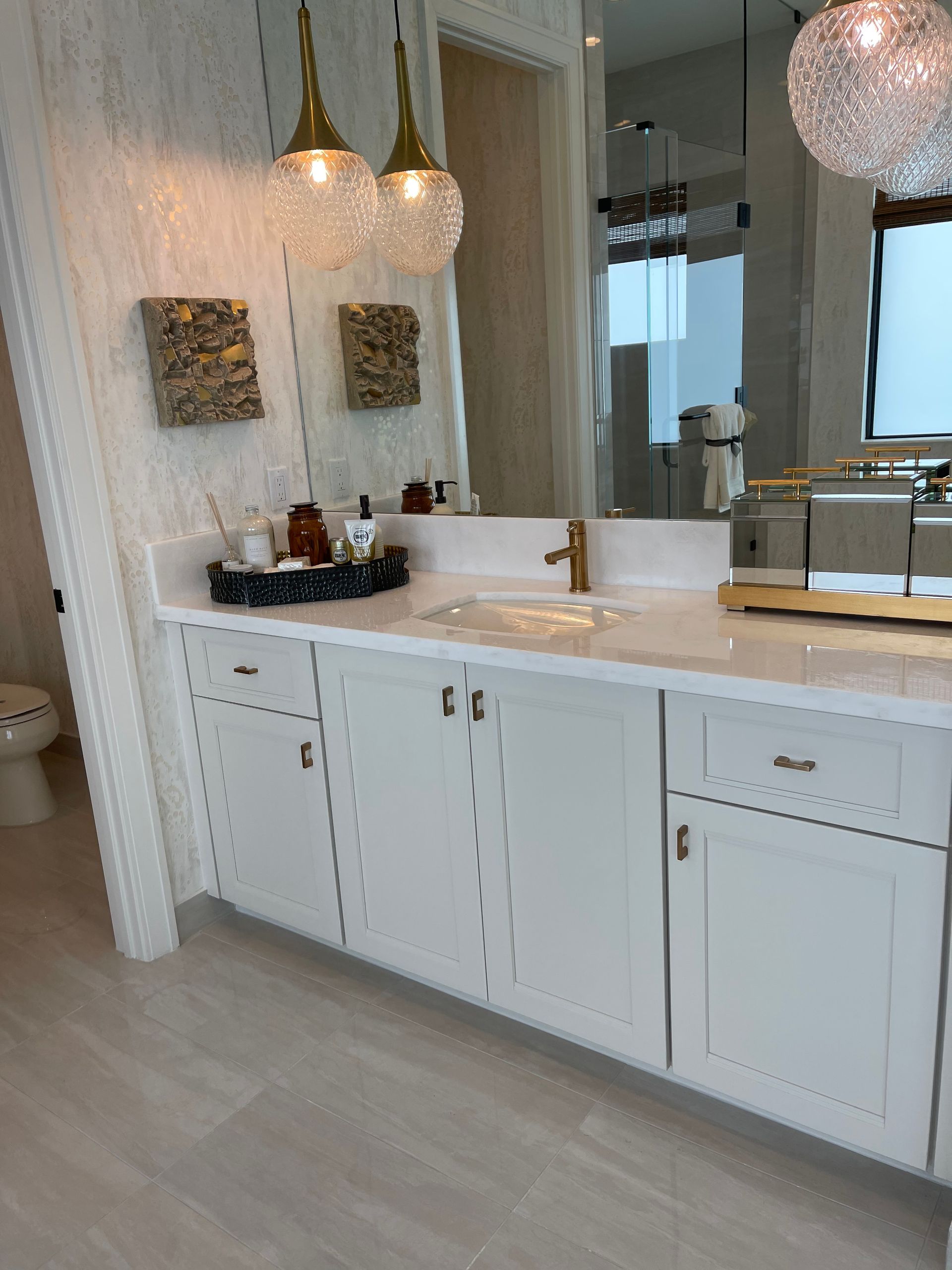 A modern white bathroom vanity with gold fixtures, two pendant lights, and a large mirror reflecting a bright space.