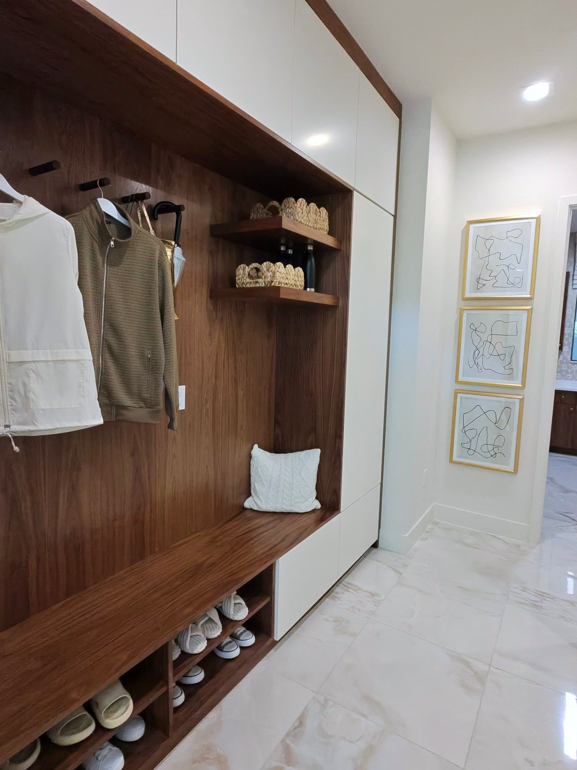 A modern mudroom entryway featuring a walnut wood bench with built-in shoe storage, coat hooks, and white cabinetry.