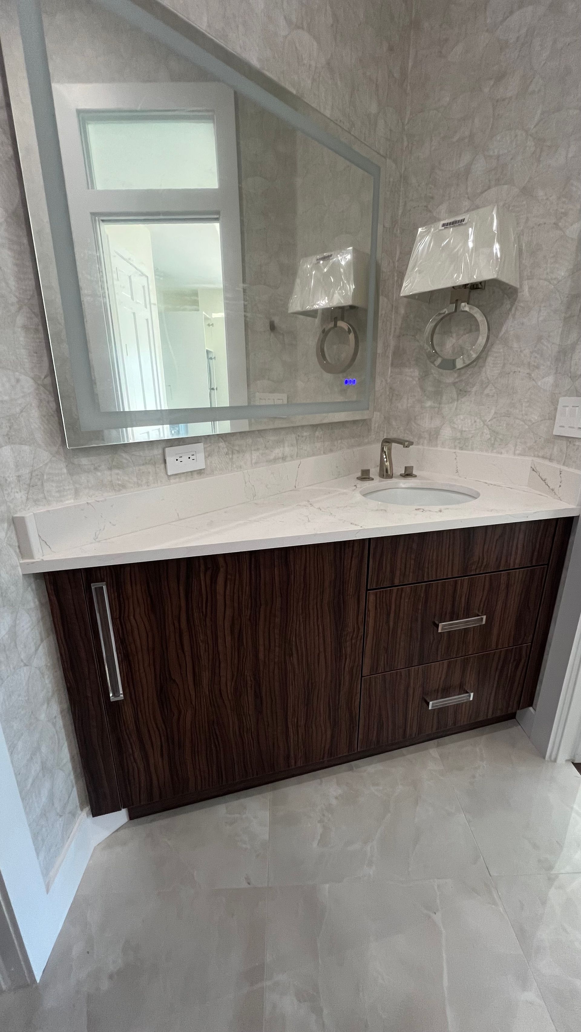 A modern bathroom vanity with a dark wood cabinet, white stone countertop, a large framed mirror, and two wall sconces.