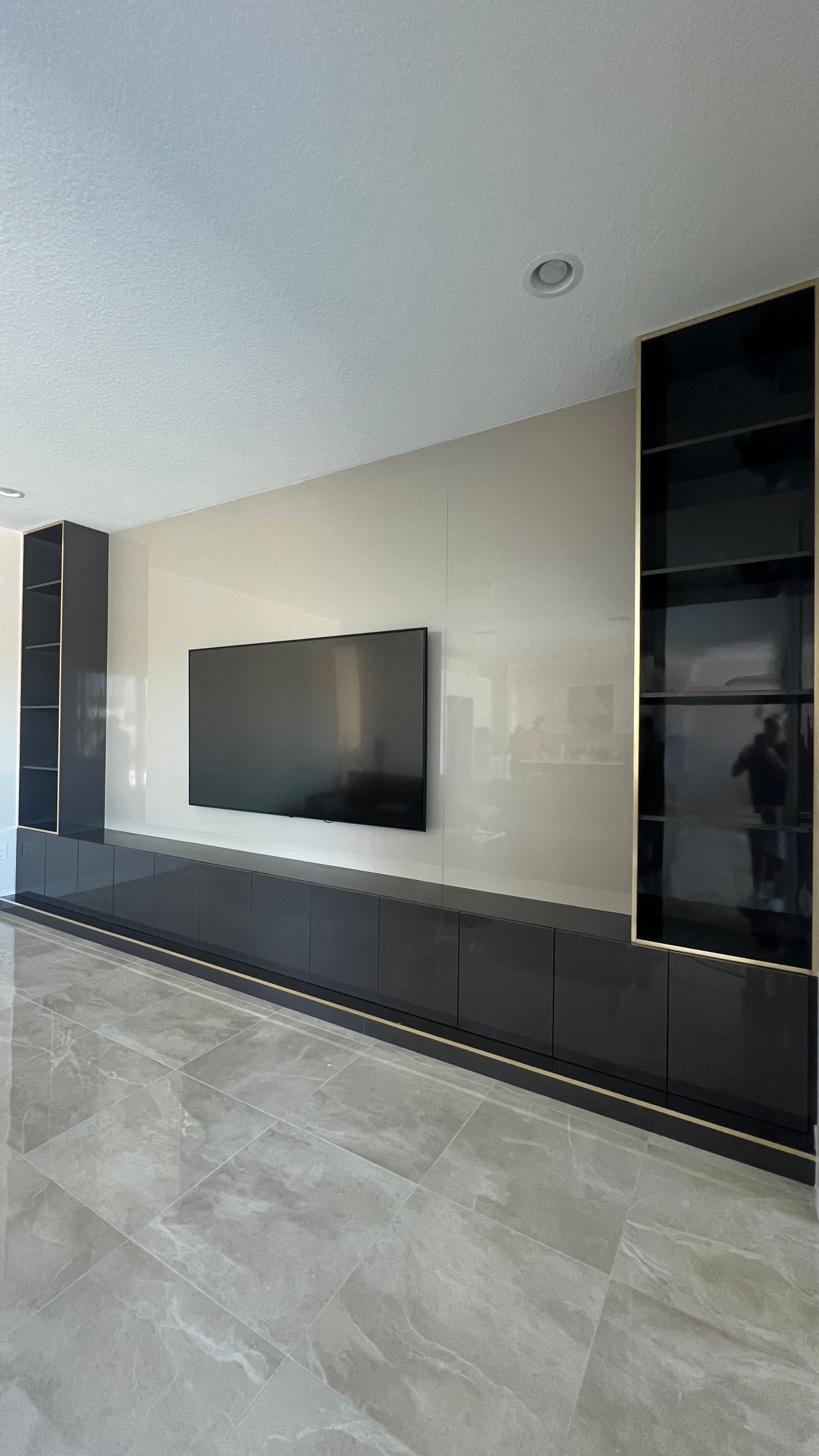 A wall-mounted TV flanked by two dark, glass-fronted shelving towers over a sleek, low-profile black media console.