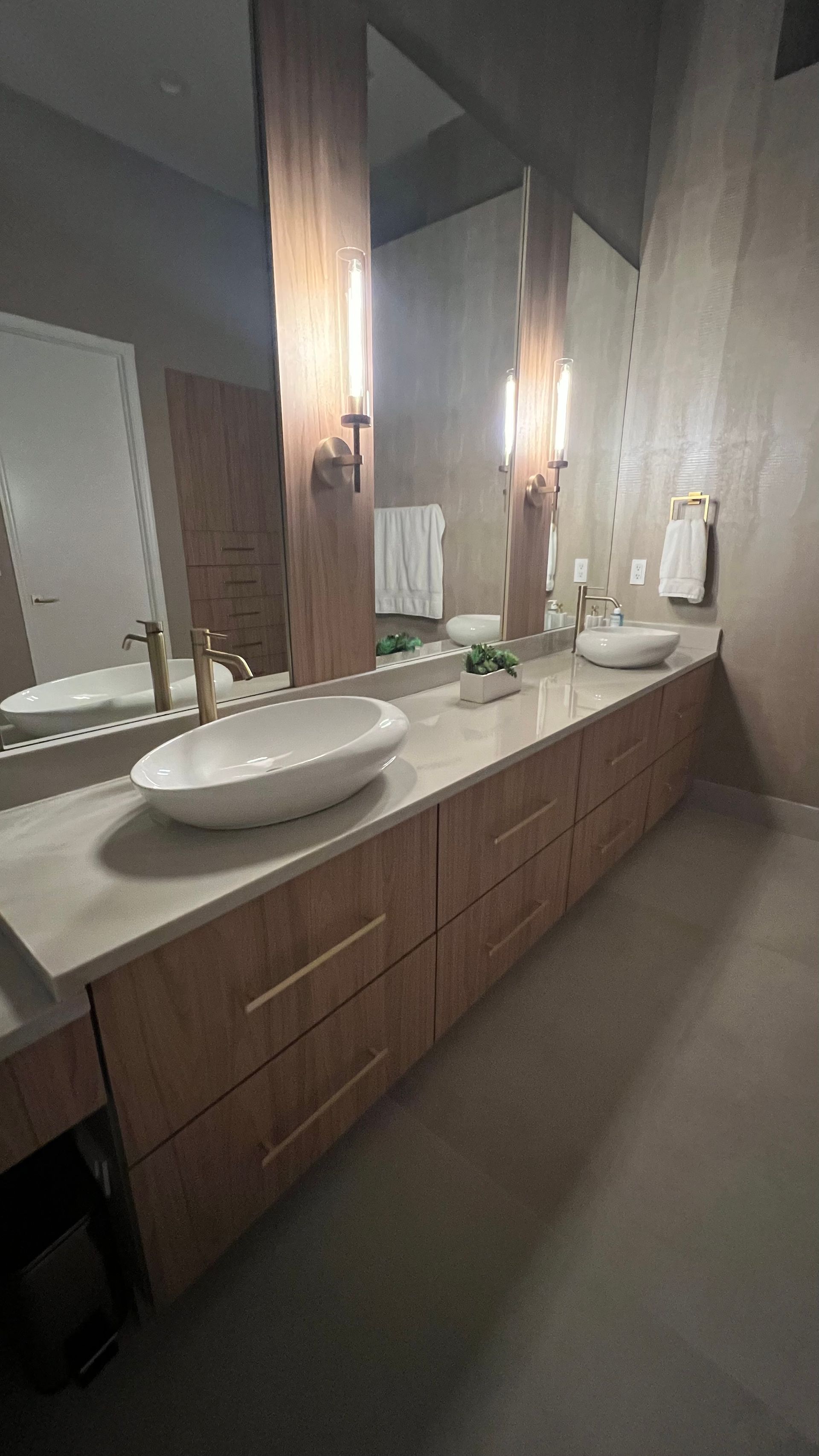A modern double-sink bathroom vanity with light wood cabinetry, white stone countertop, and two oval vessel sinks.
