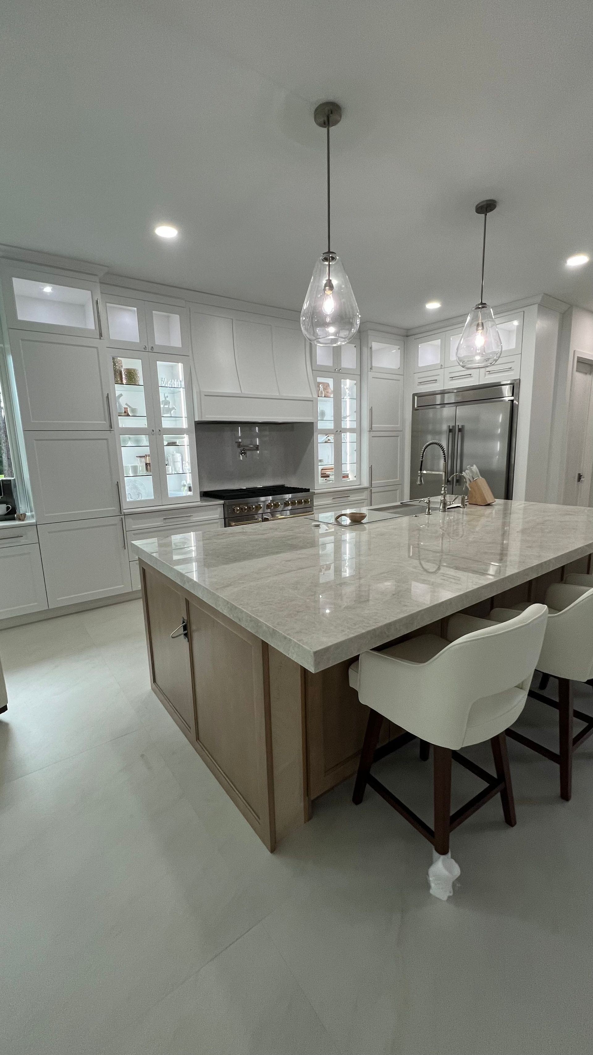 A modern kitchen featuring a large island with white stone countertops, wooden cabinetry, and two pendant lights.