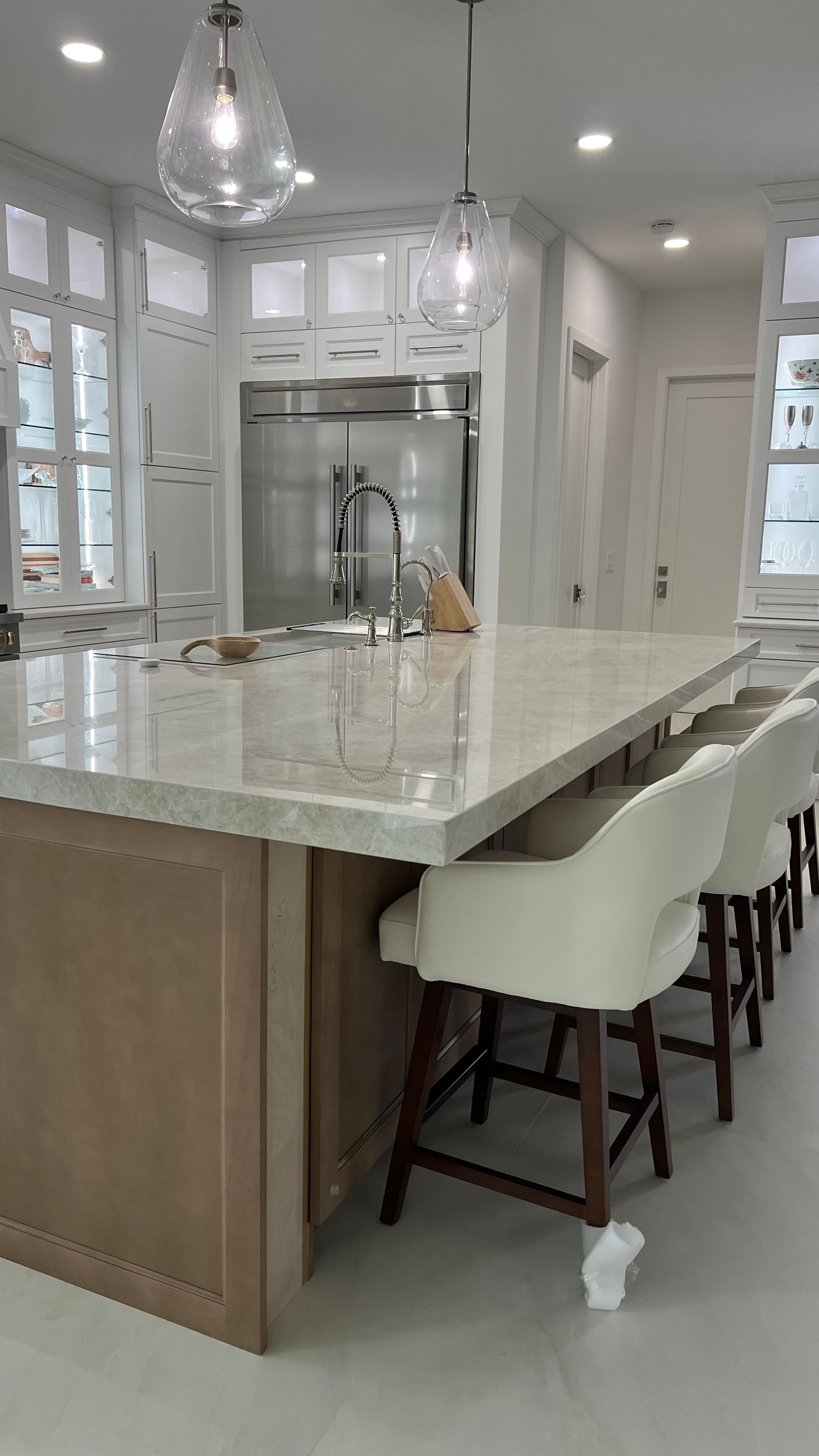 A modern kitchen island with light wood cabinetry, a quartz countertop, and three white stools under pendant lights.