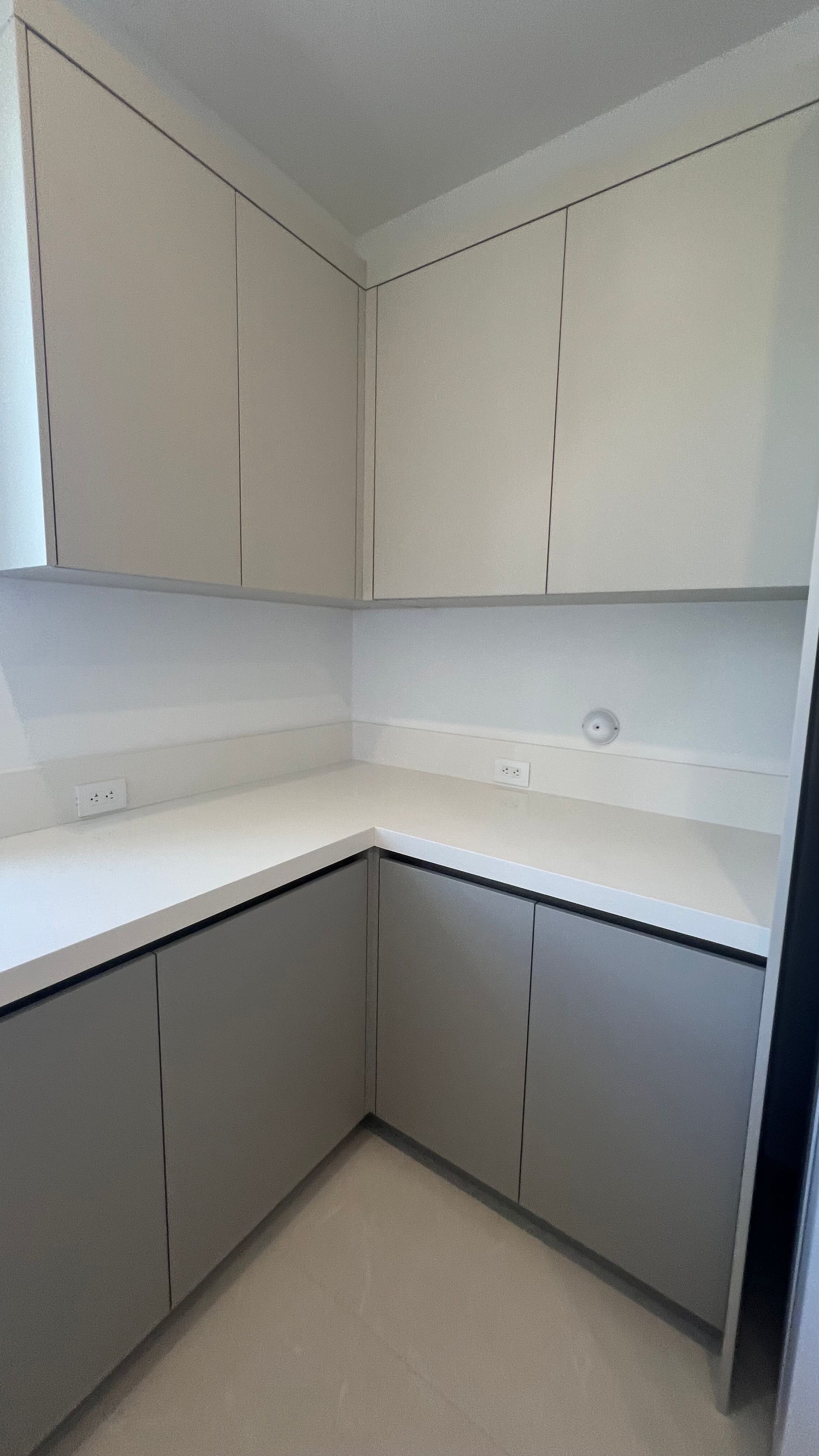 A kitchen corner with light grey lower cabinets, white upper cabinets, and a white countertop.