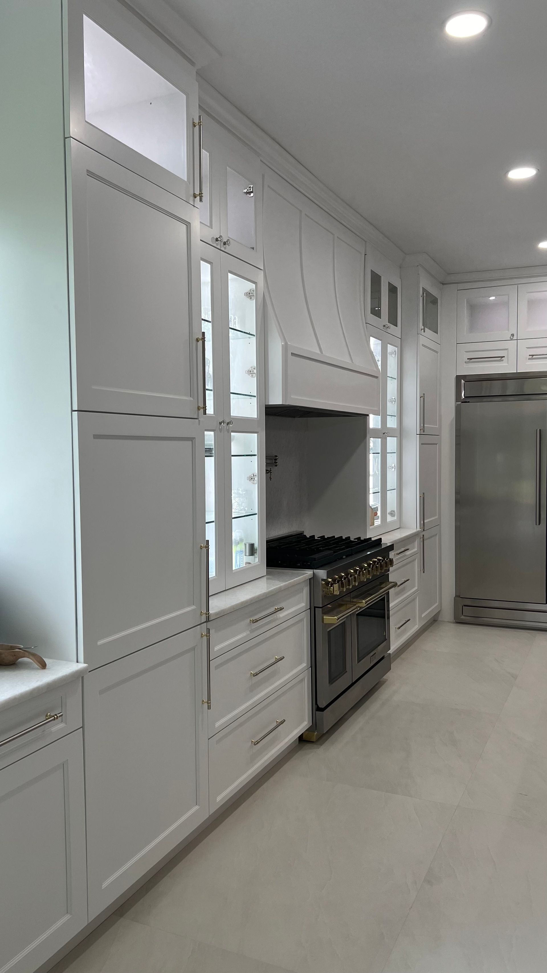 A bright, modern kitchen featuring white floor-to-ceiling cabinets, a stainless steel range, and a large refrigerator.