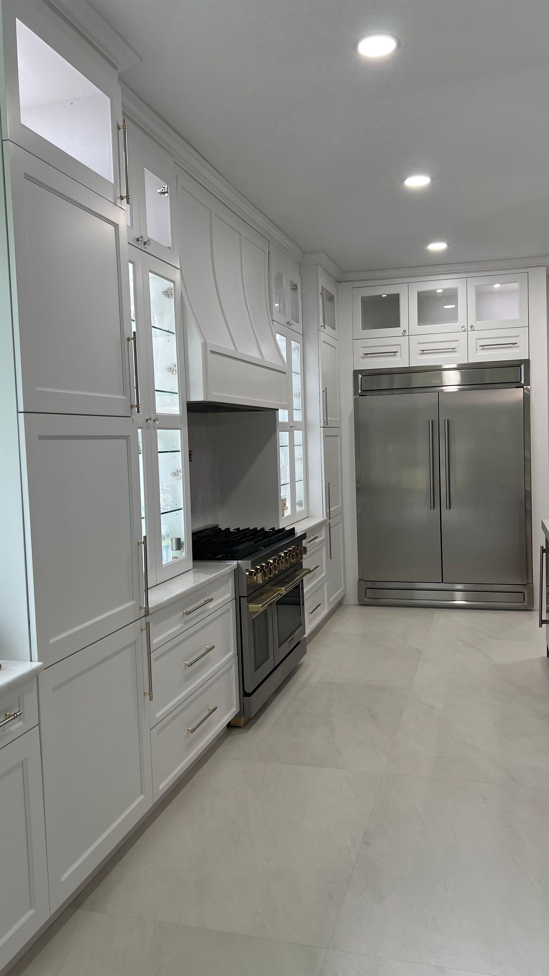 A modern, bright white kitchen featuring floor-to-ceiling cabinetry, a professional-style range, and a large metal fridge.