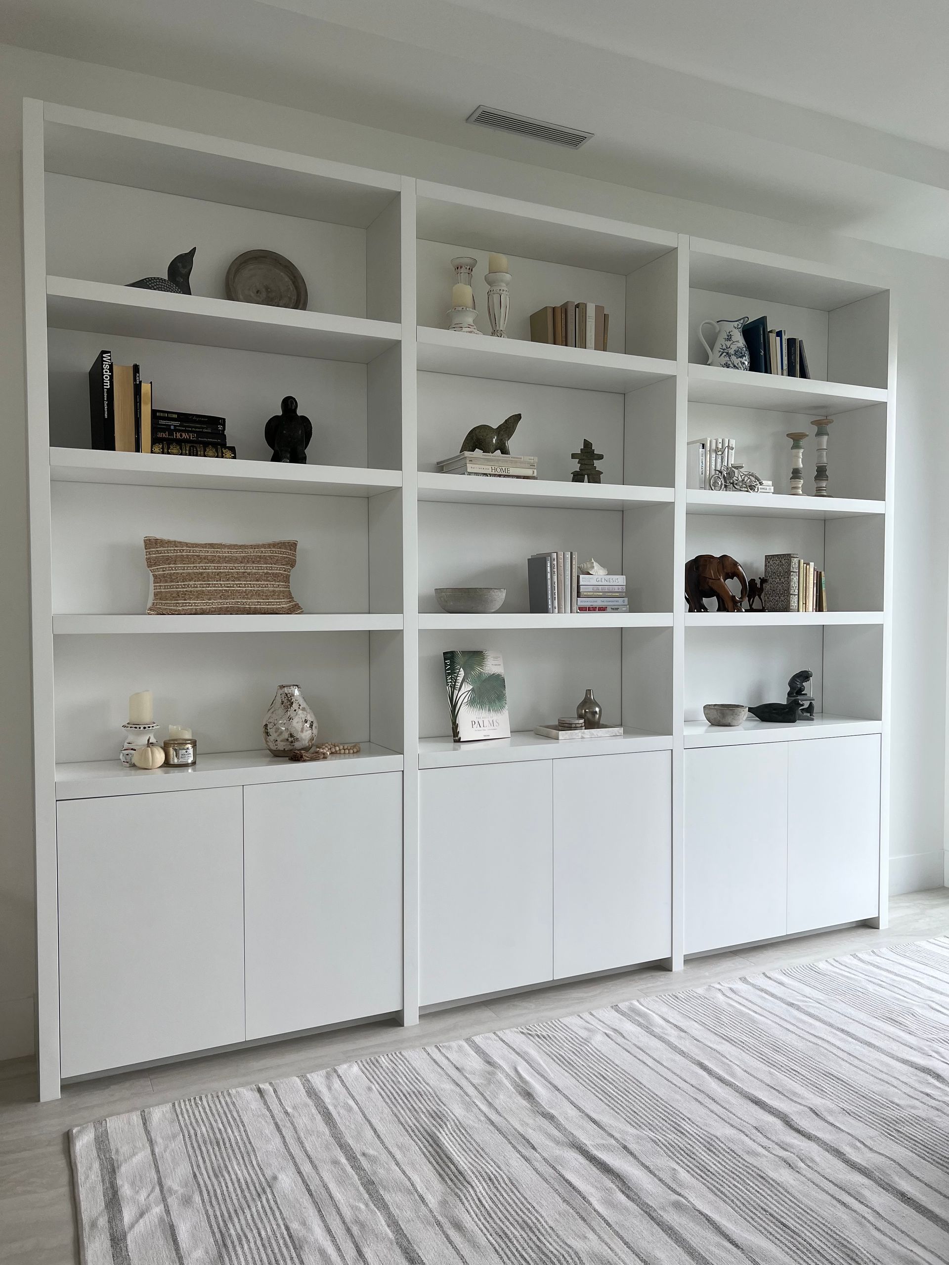 A large, white, built-in bookshelf featuring open shelving above and closed storage cabinets at the base.