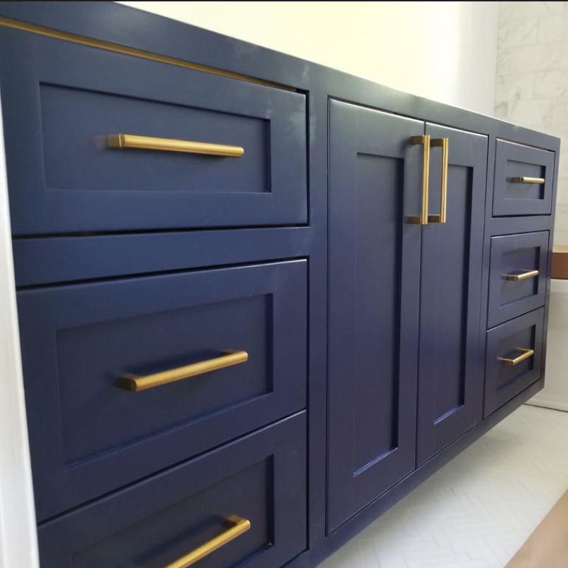 A navy blue bathroom vanity with Shaker-style cabinet doors and drawers accented by horizontal gold hardware.