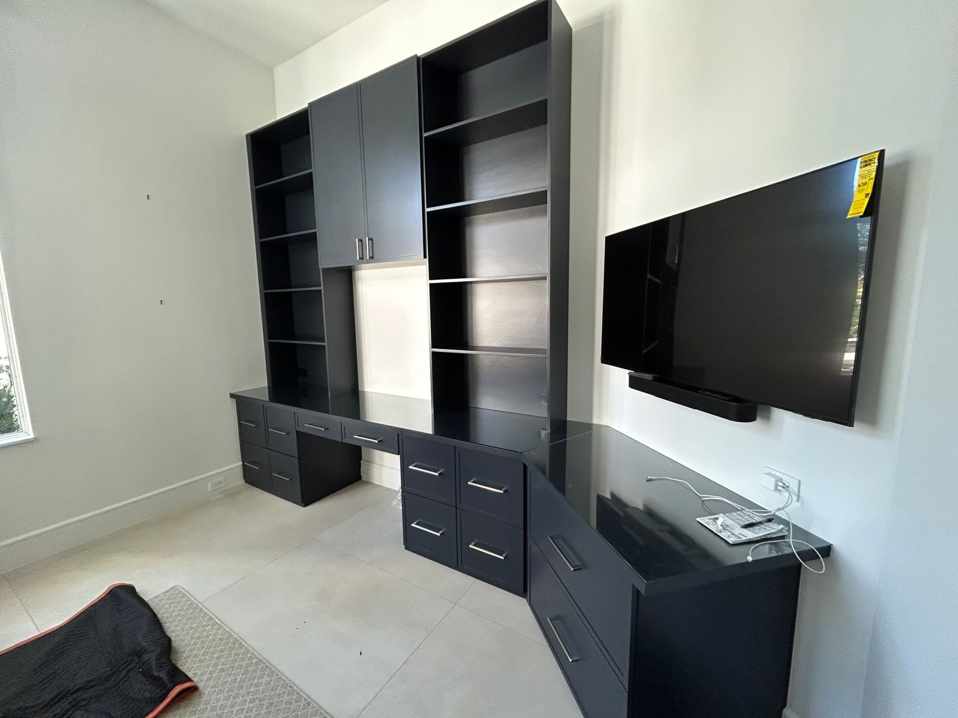 A dark, built-in desk and shelving unit with drawers and cabinets in a room with a wall-mounted flat-screen television.