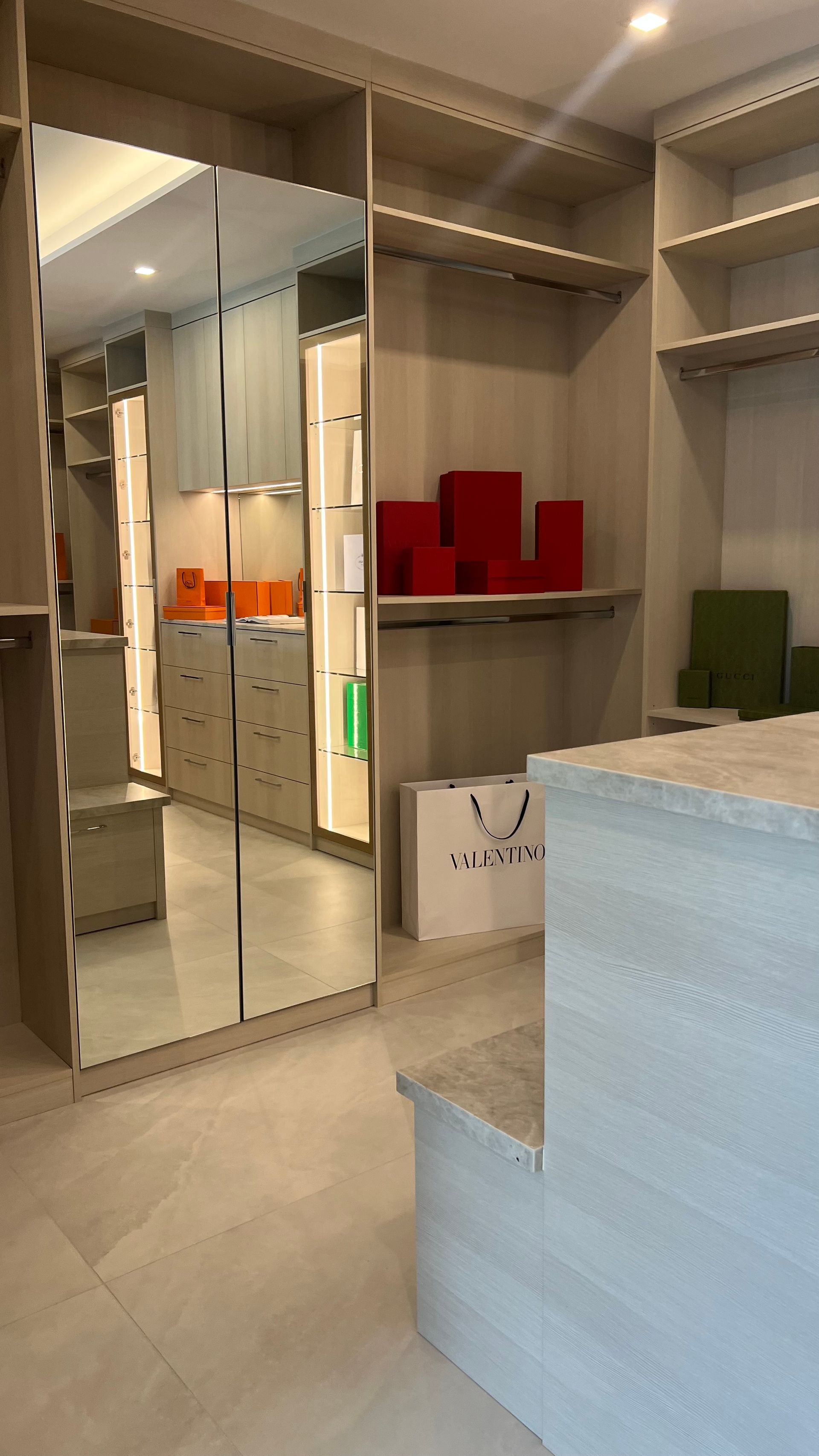 A modern walk-in closet featuring light wood cabinetry, a tall mirror, open shelving, and a large central island.