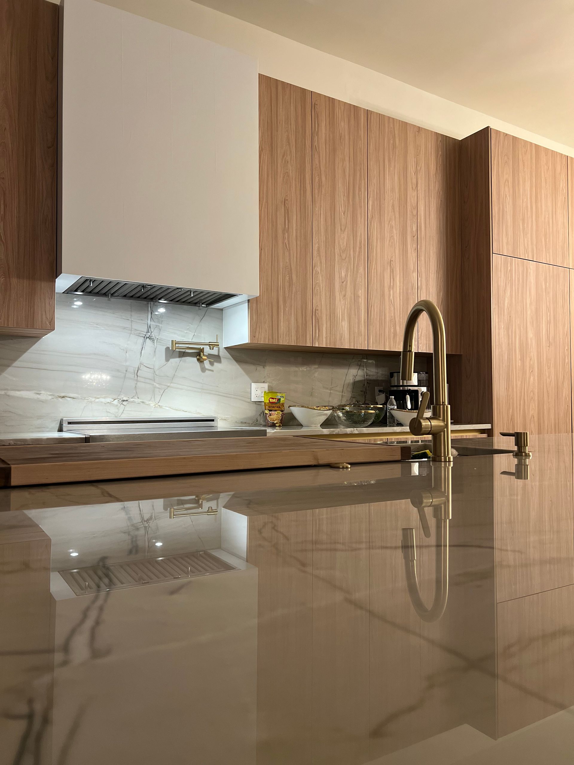 A modern kitchen with wood cabinets, a white marble backsplash, and a gold faucet on a polished stone countertop.