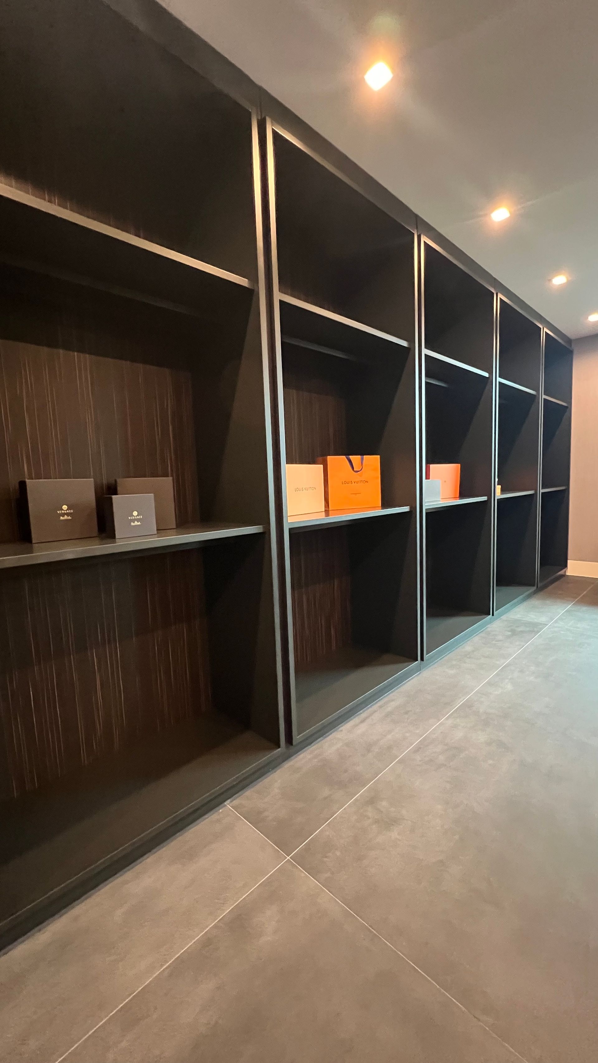A perspective view of large, dark wooden display shelving holding a few orange and neutral-colored shopping bags.