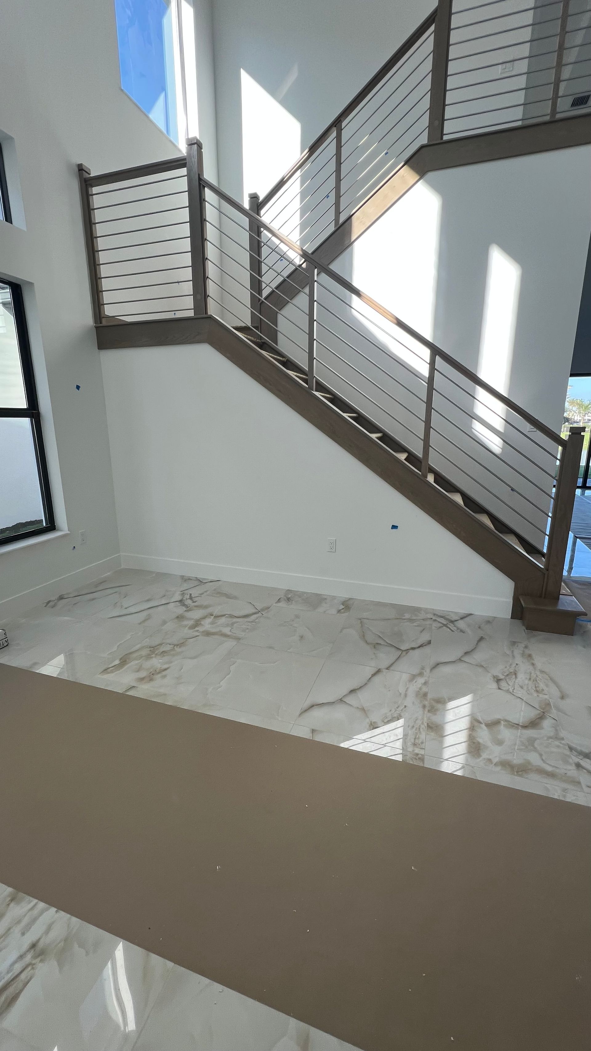 A modern staircase with a wooden frame and cable railing, set against white walls and a white marble-look tile floor.