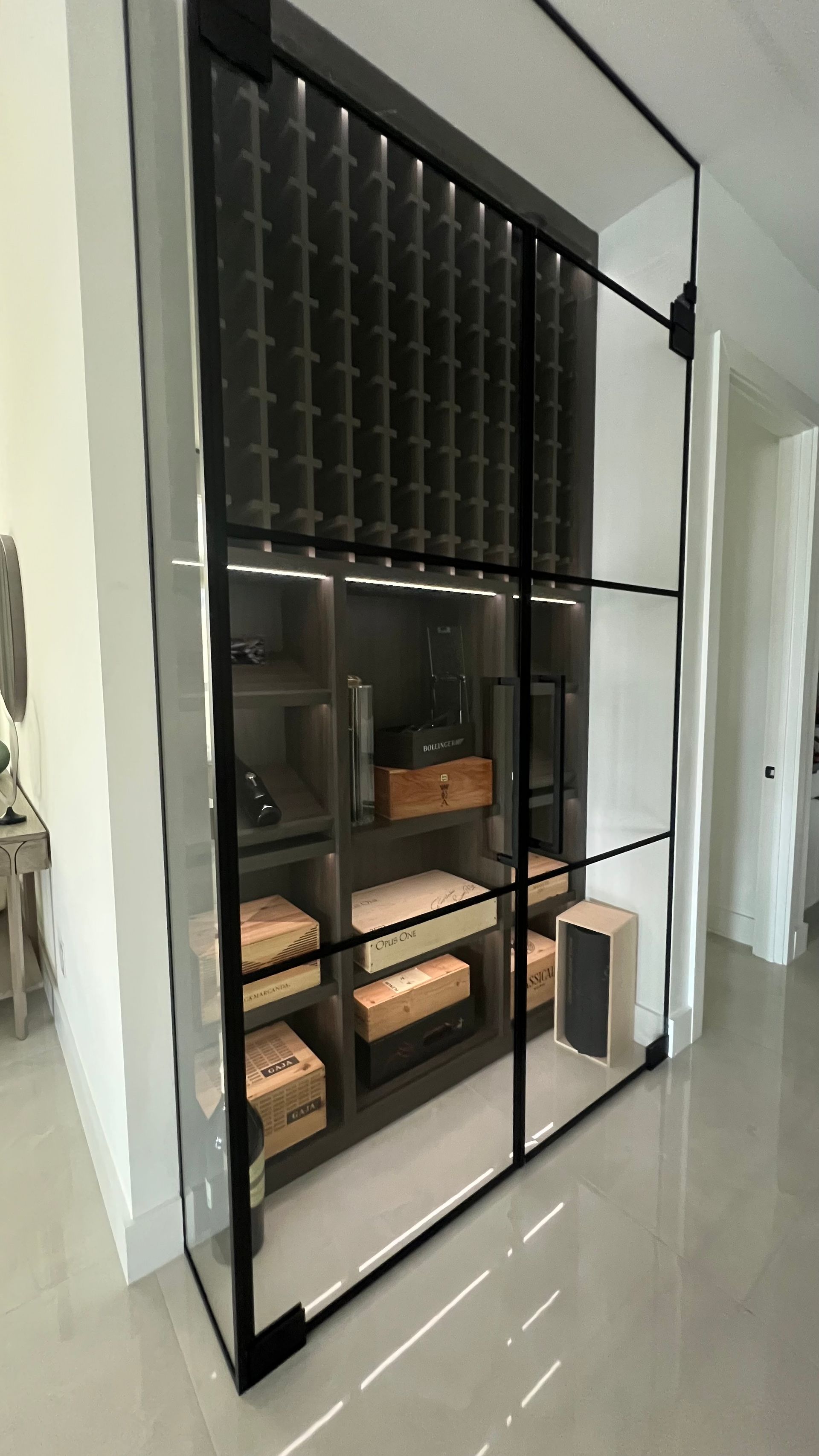 A tall, modern floor-to-ceiling glass display cabinet with black frames, showcasing interior shelves and lighting.