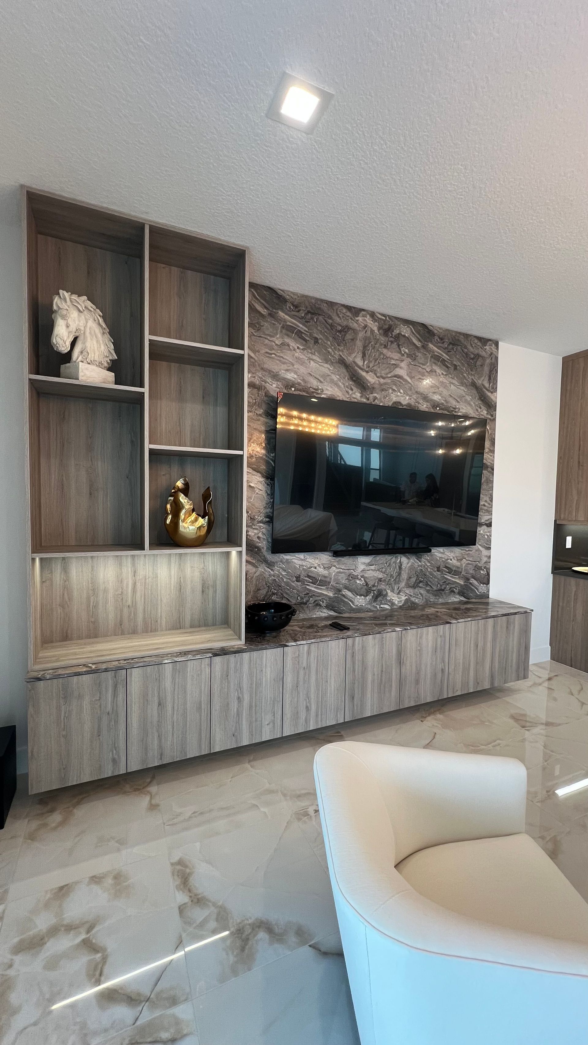 A modern living room features a TV mounted on a marble accent wall, integrated wood shelving, and a floating cabinet.