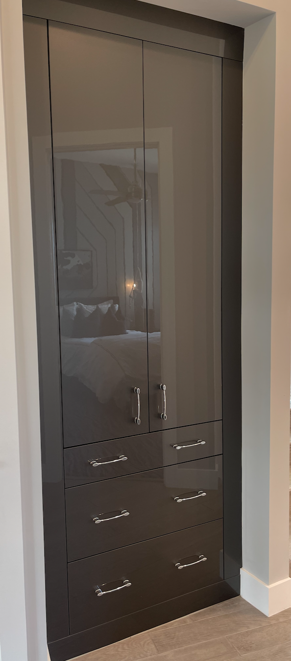 Dark, glossy built-in cabinet with two upper doors and three lower drawers, set into a wall in a room.