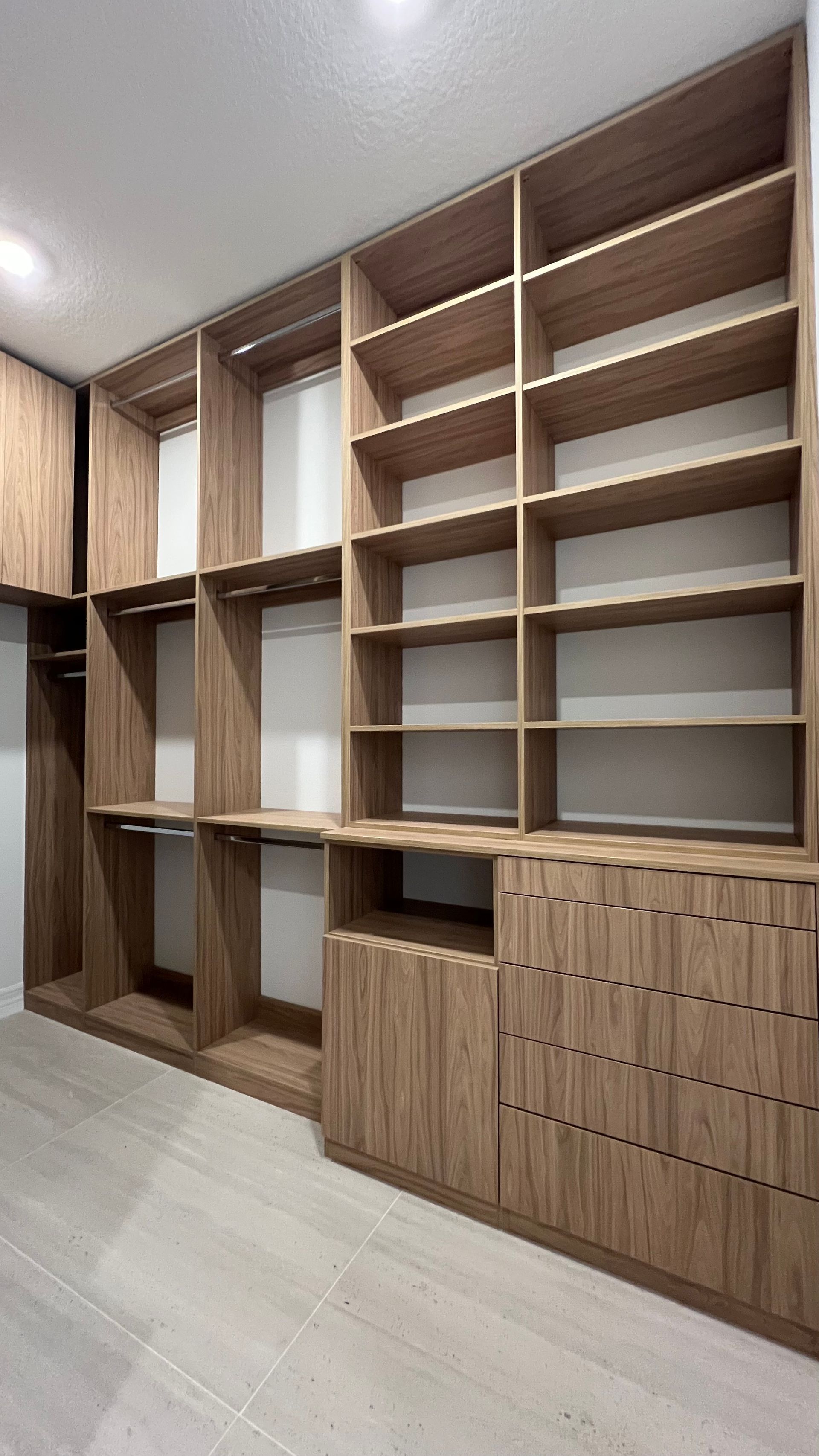 Custom wooden walk-in closet shelving unit featuring open hanging sections and lower cabinet drawers on a tiled floor.