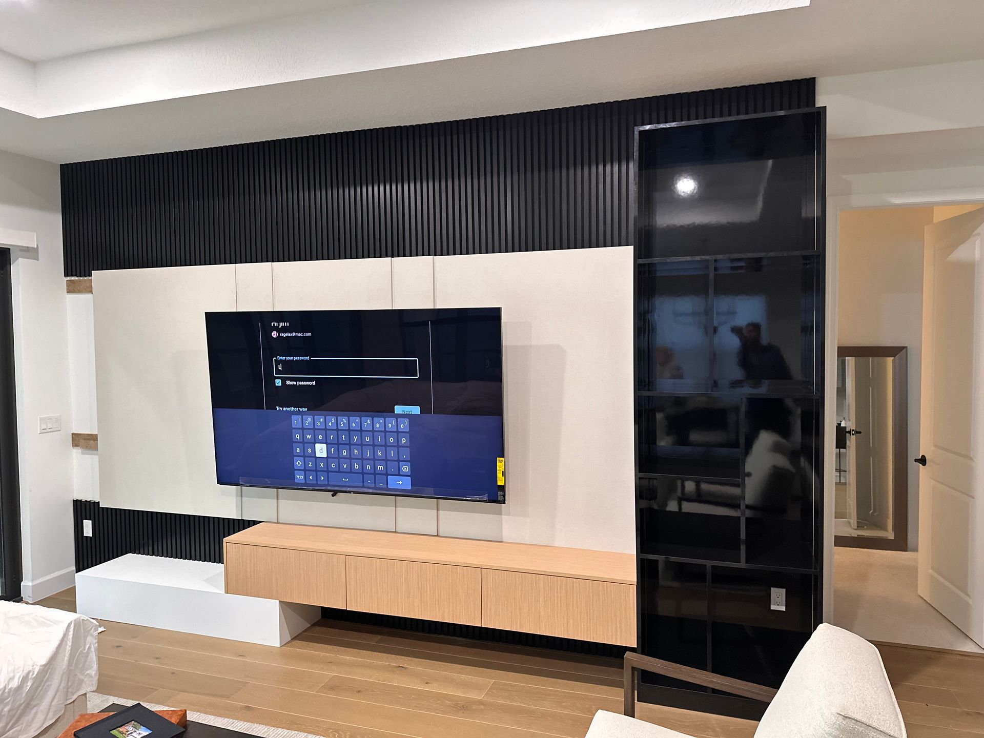 Modern wall unit with a mounted TV, light wood floating cabinet, white base, and a tall black glass display cabinet.