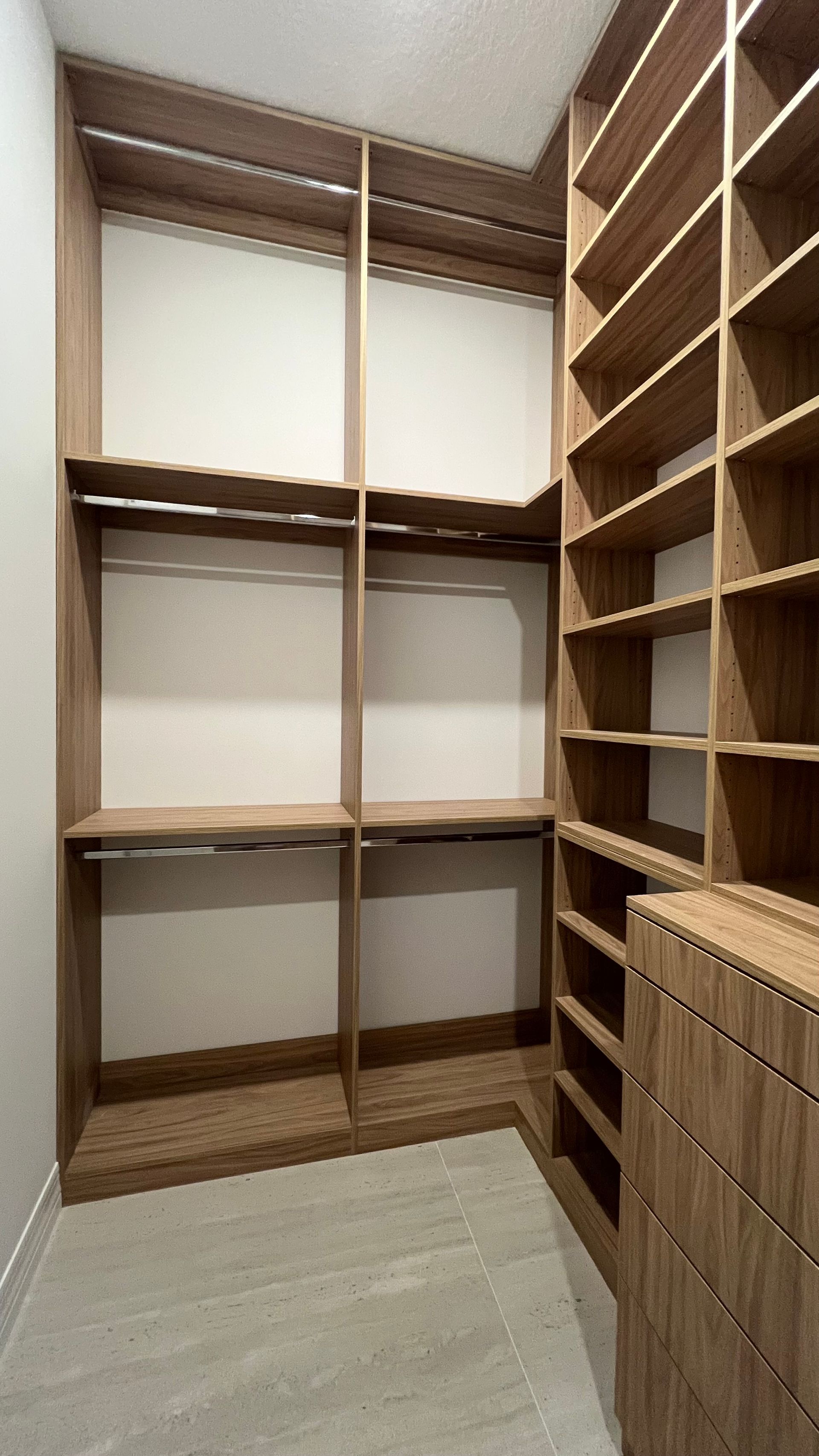 A walk-in closet with light wood shelving, hanging rods, and a stack of drawers on a light-colored tile floor.