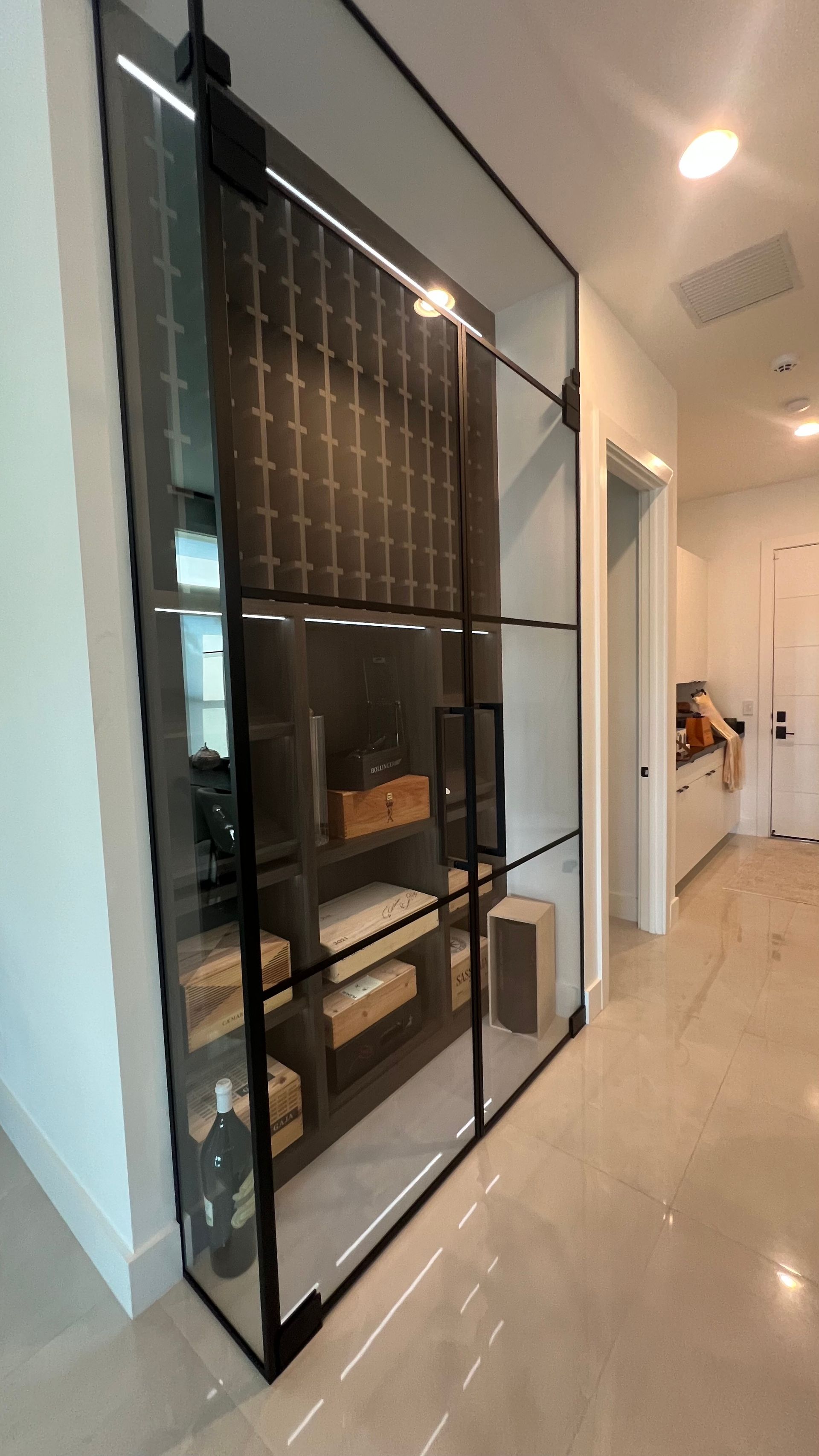 A sleek, floor-to-ceiling glass-paneled display case with black framing and interior shelving in a modern home hallway.