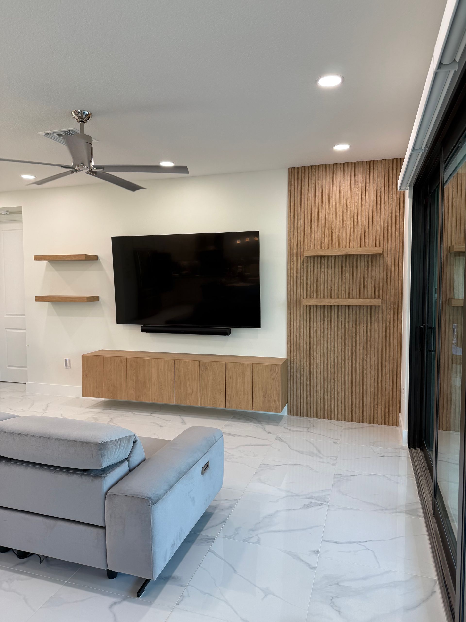 Modern living room with a gray sofa, floating wood media console, wall-mounted TV, and decorative slatted wood accent wall.