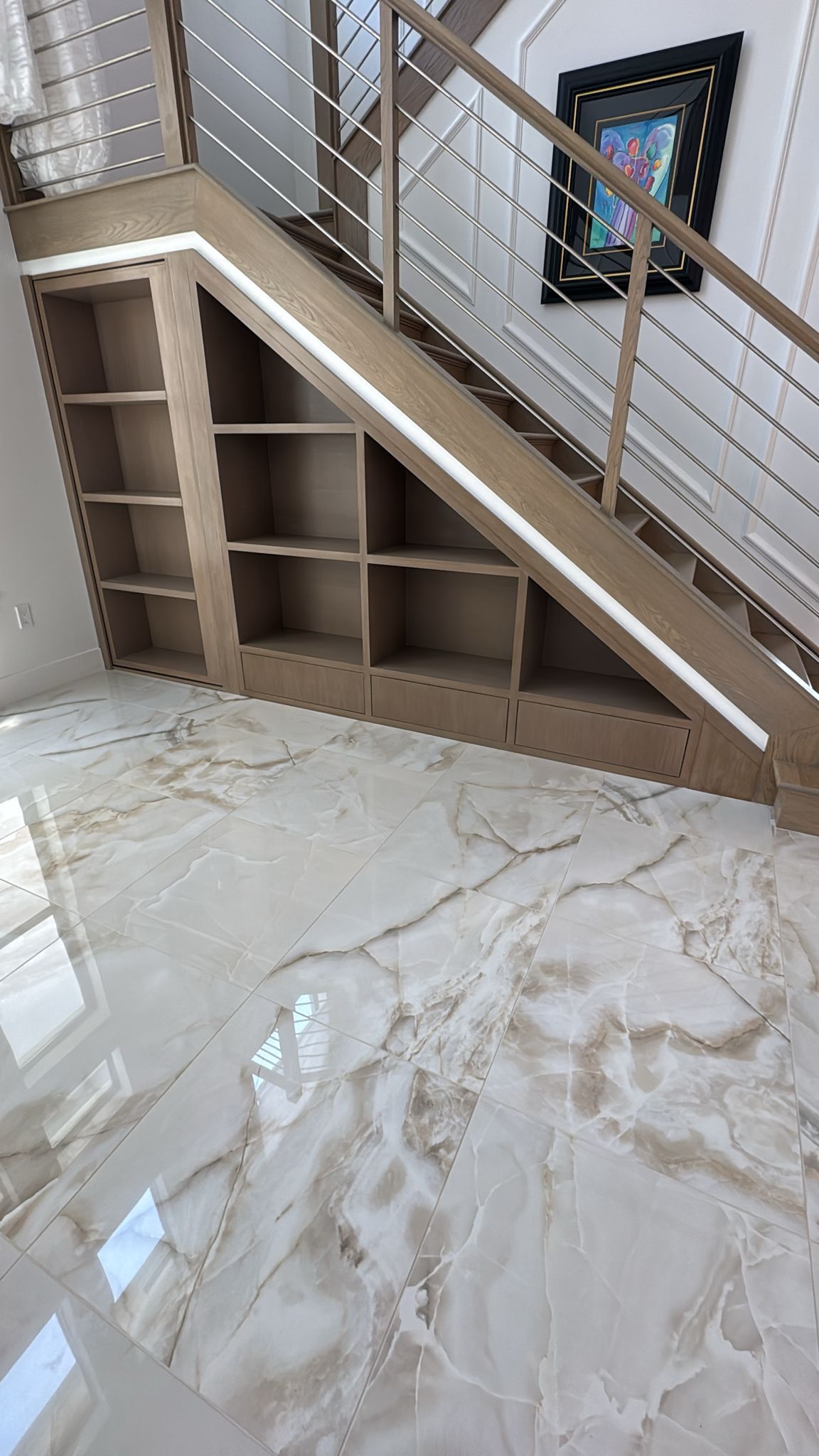 A staircase with integrated wooden storage shelves built underneath, set against light marble flooring and a wall mirror.