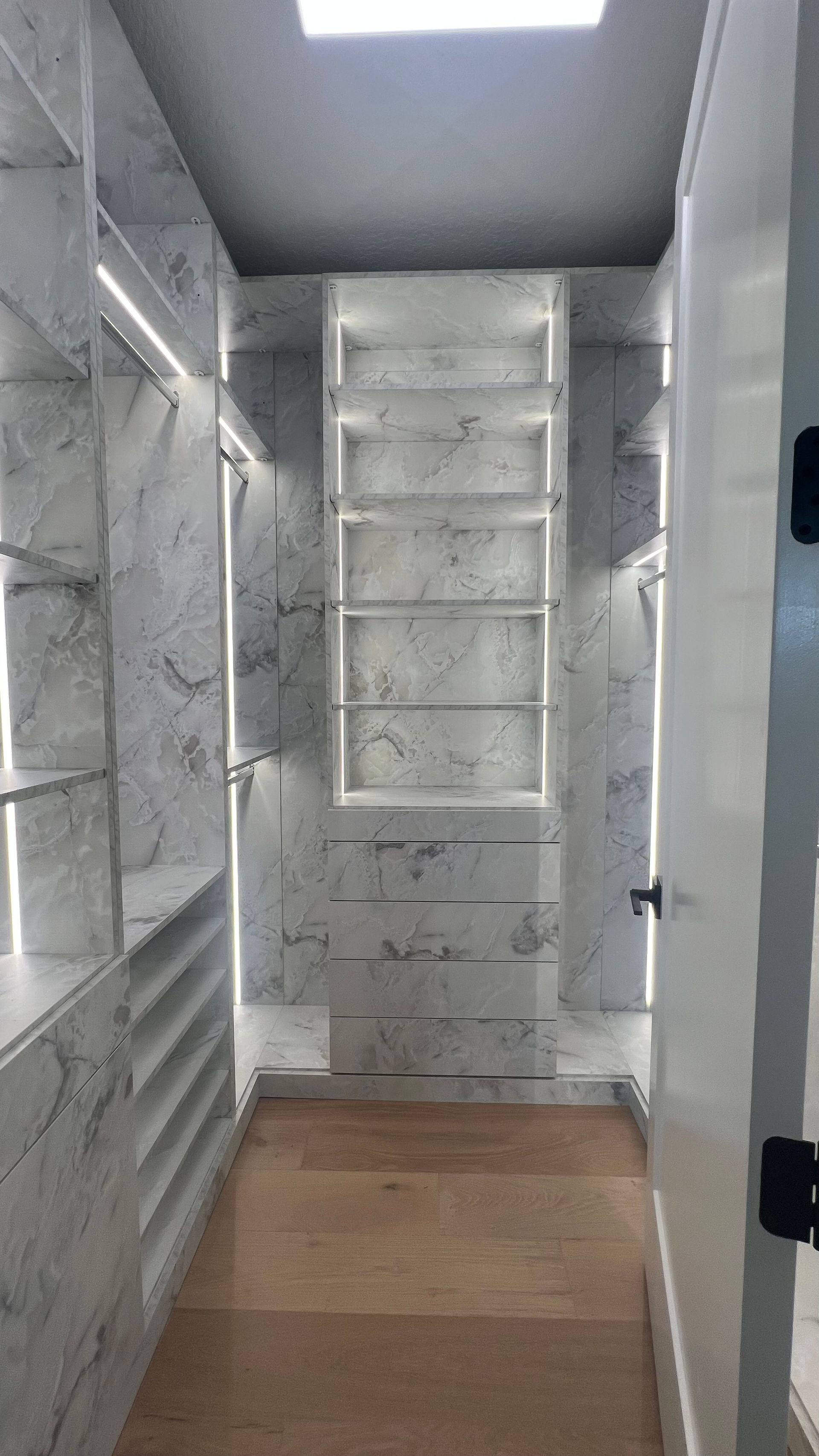 Walk-in closet featuring white marble shelves, integrated LED lighting, and light-toned wooden flooring.