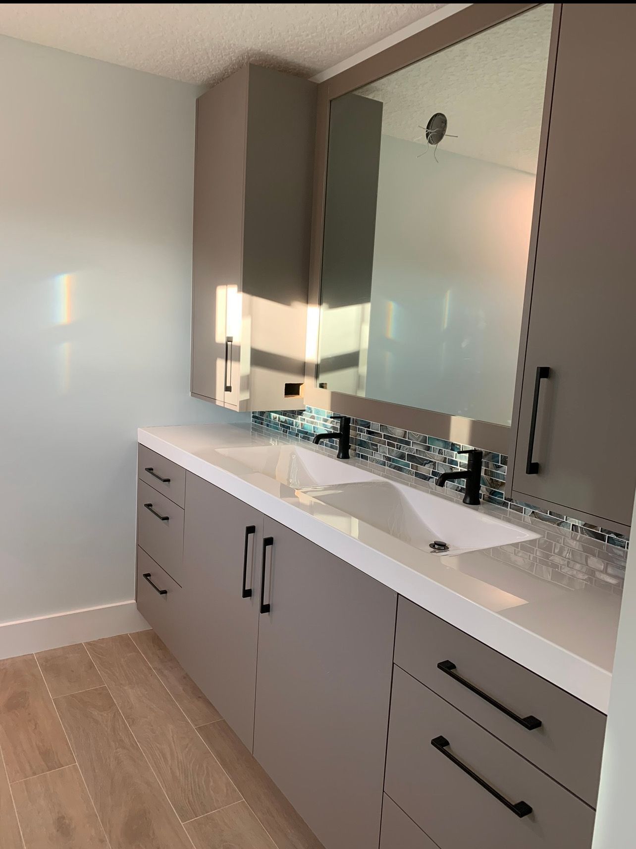 A modern bathroom vanity with gray cabinets, a double sink, black hardware, a tiled backsplash, and a large mirror.