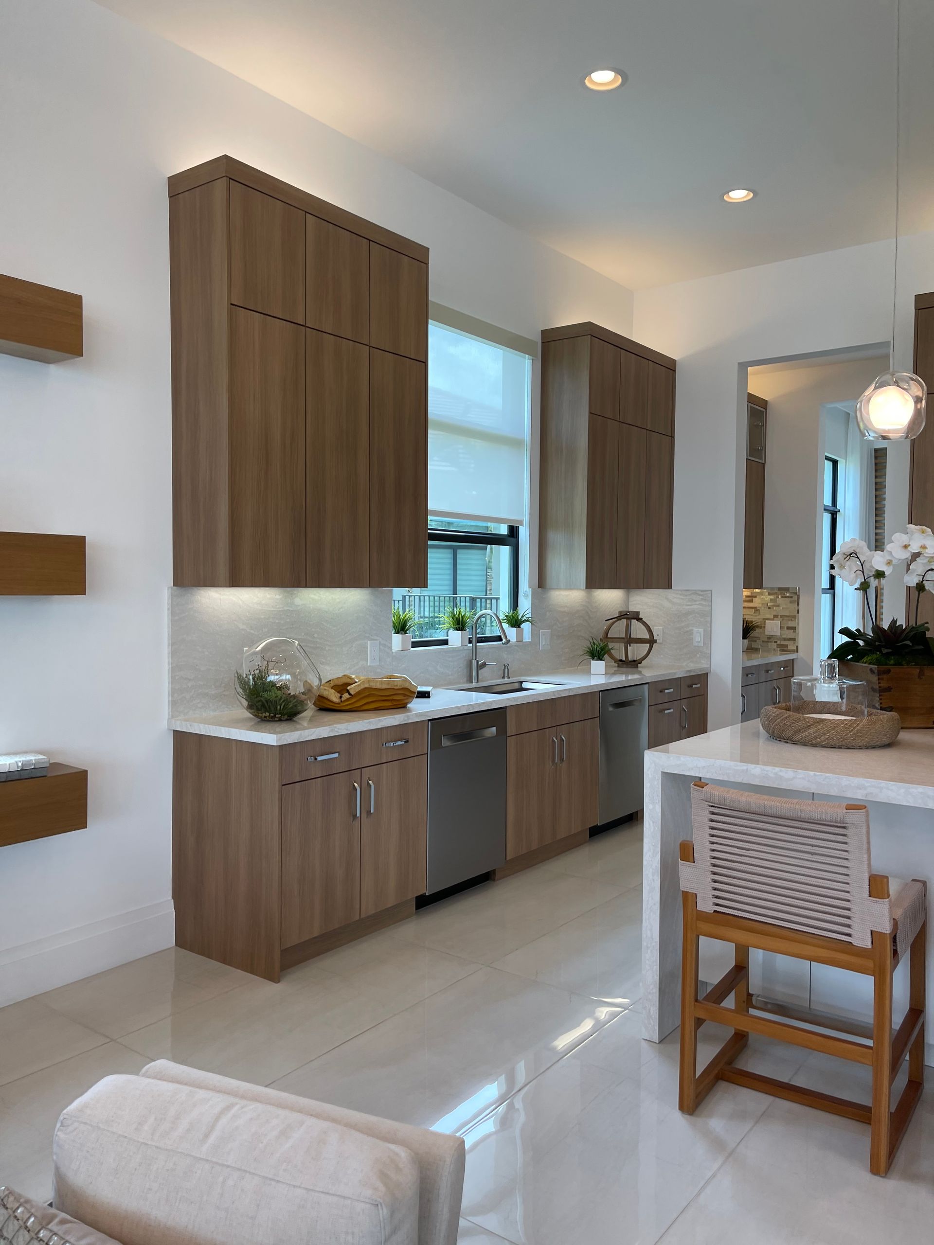 Modern kitchen with flat-panel brown wood cabinets, light countertops, stainless appliances, and a bar-height island chair.