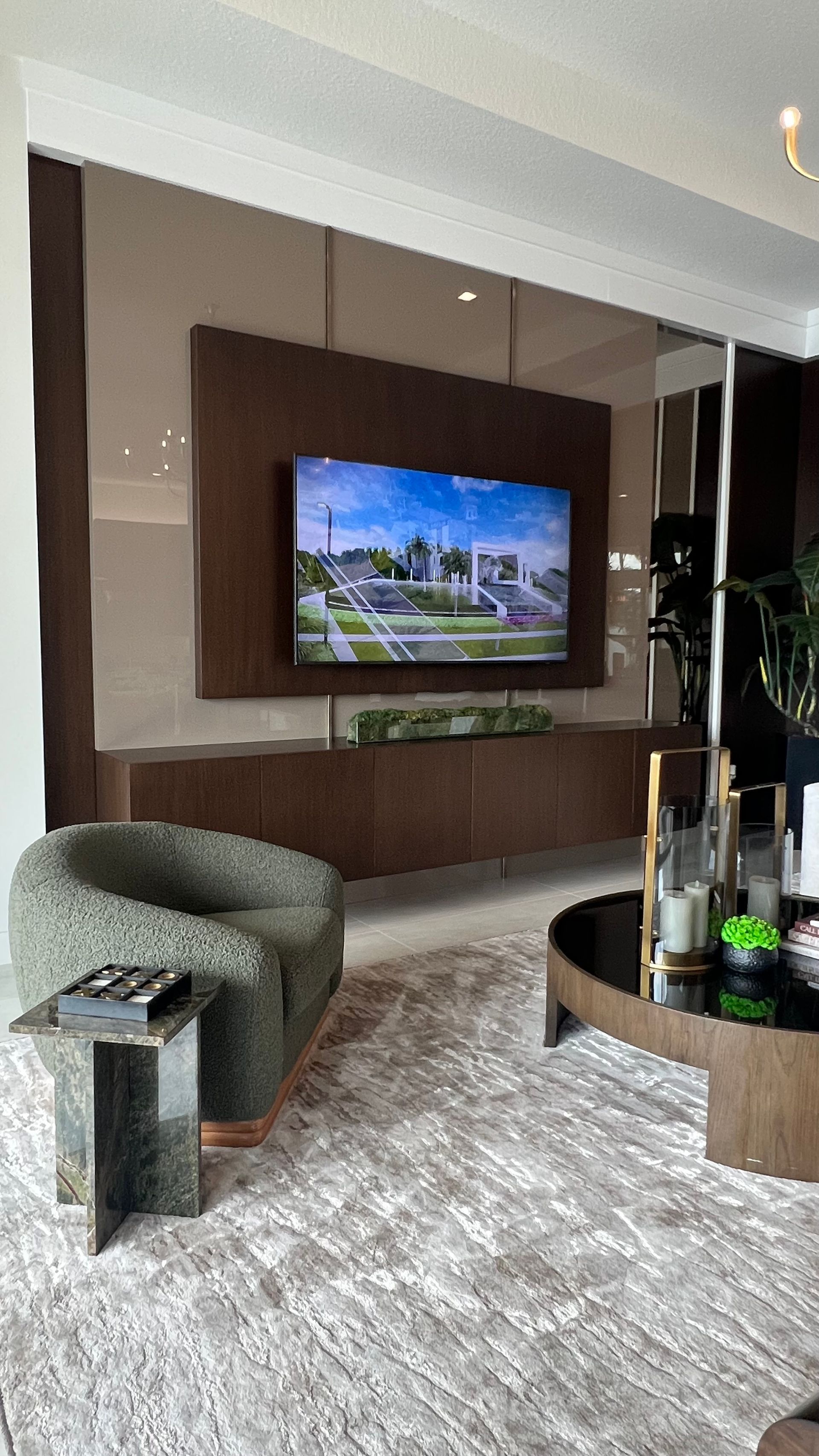 A modern living room with a brown accent wall, wall-mounted television, wooden console, round coffee table, and arm chair.