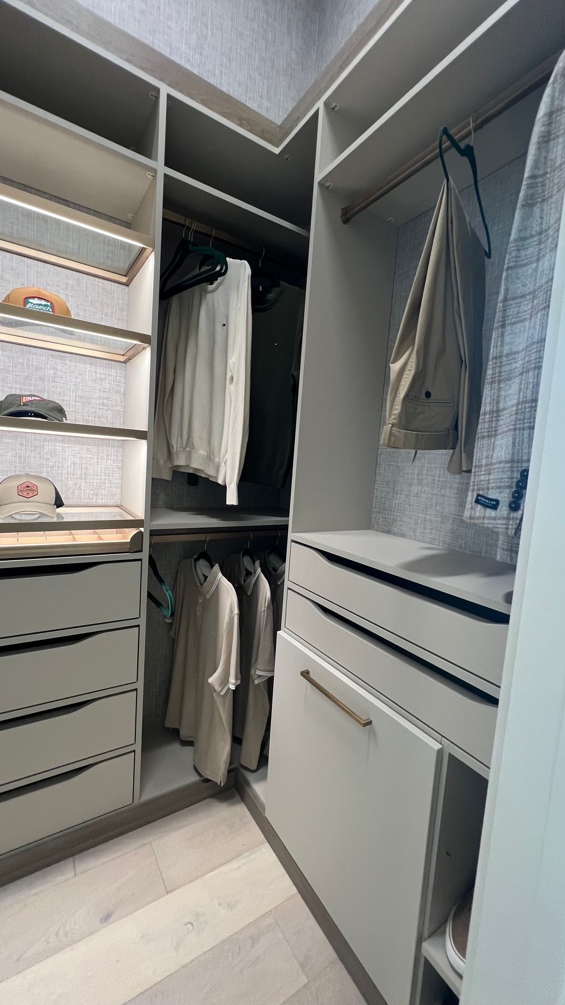 A well-organized walk-in closet featuring beige cabinetry, drawers, hanging clothes, and light wood flooring.
