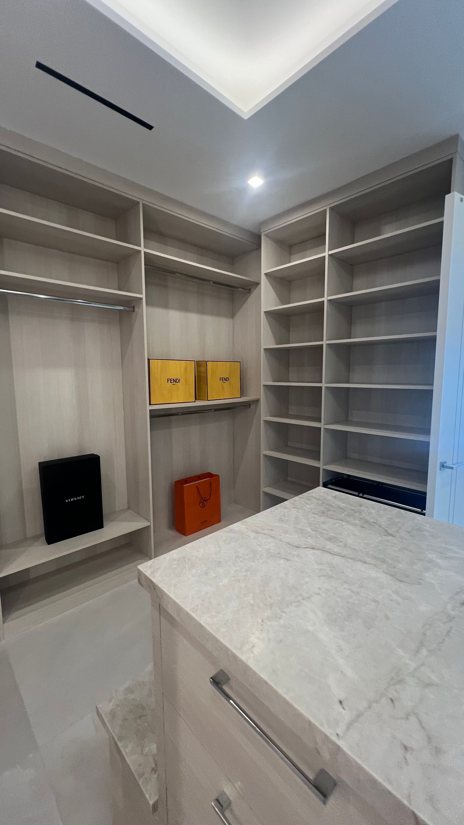 A walk-in closet with light wood shelving, a marble-topped island, and colorful storage boxes on the center shelf.