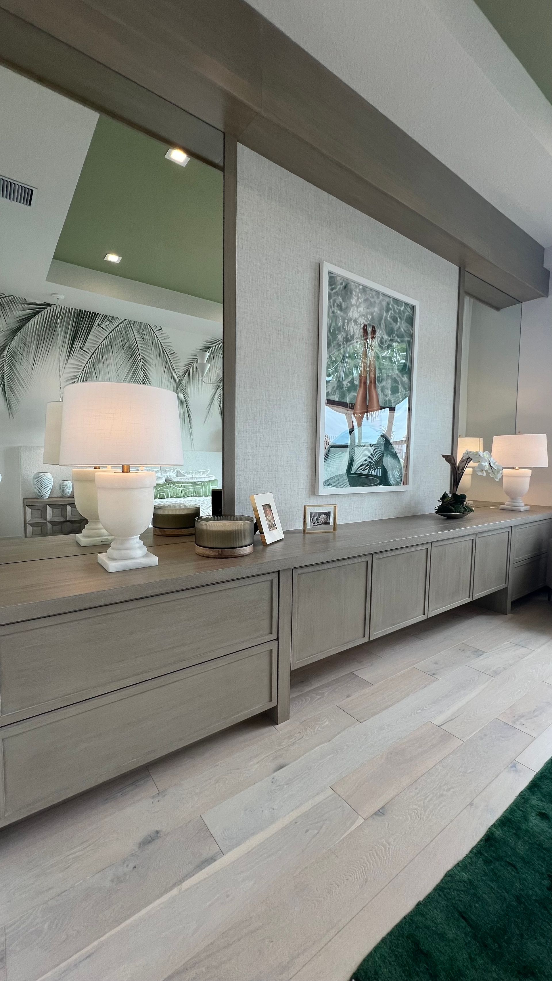 A long, light-wood console table with two lamps, a framed art print, and decor sits against a textured wall with mirrors.