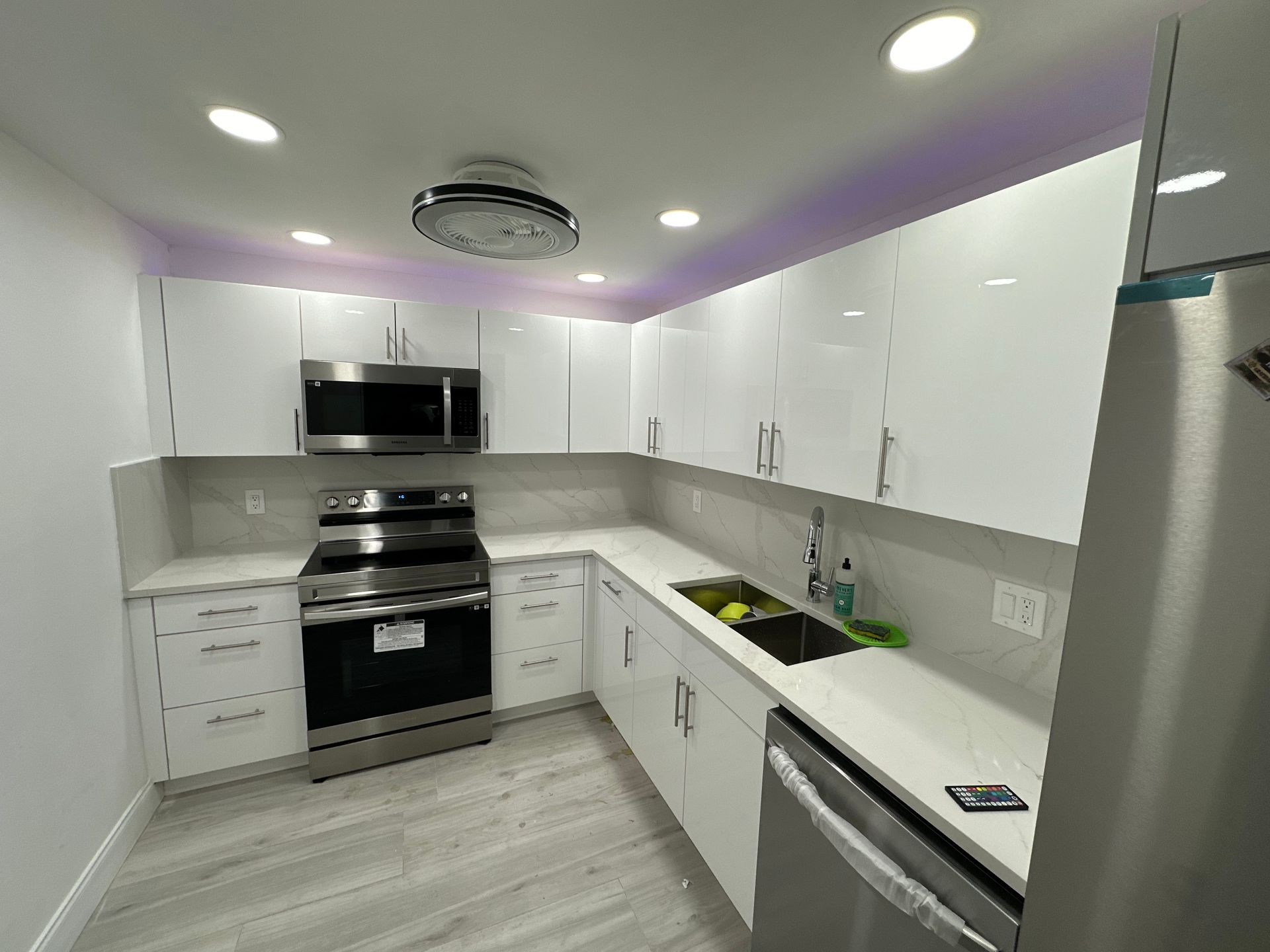 Modern kitchen with white cabinets, stainless steel appliances, white countertops, and light wood-look flooring.