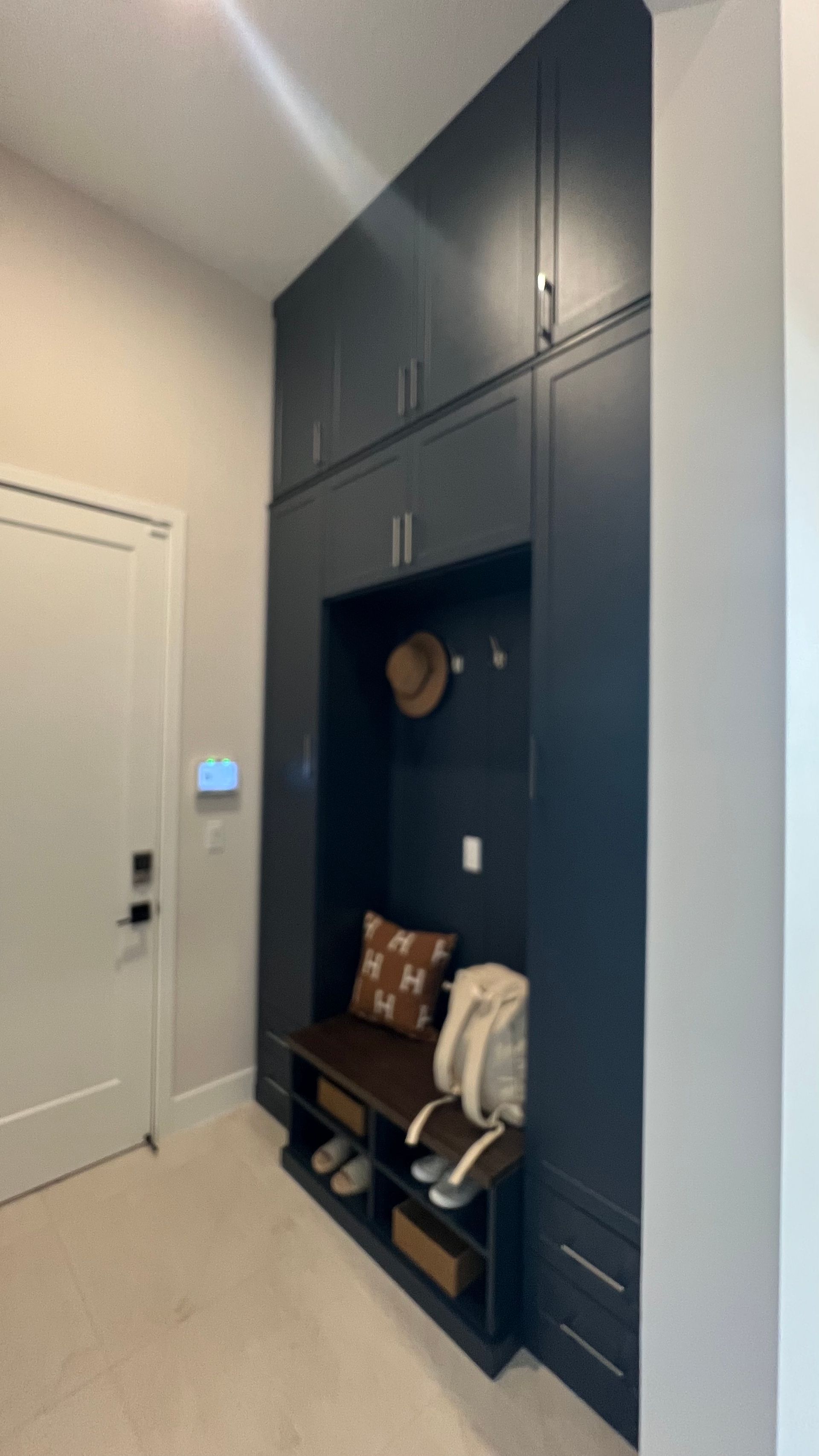 A dark blue built-in mudroom unit with overhead cabinets, open coat hooks, a bench seat with shoe storage, and side drawers.