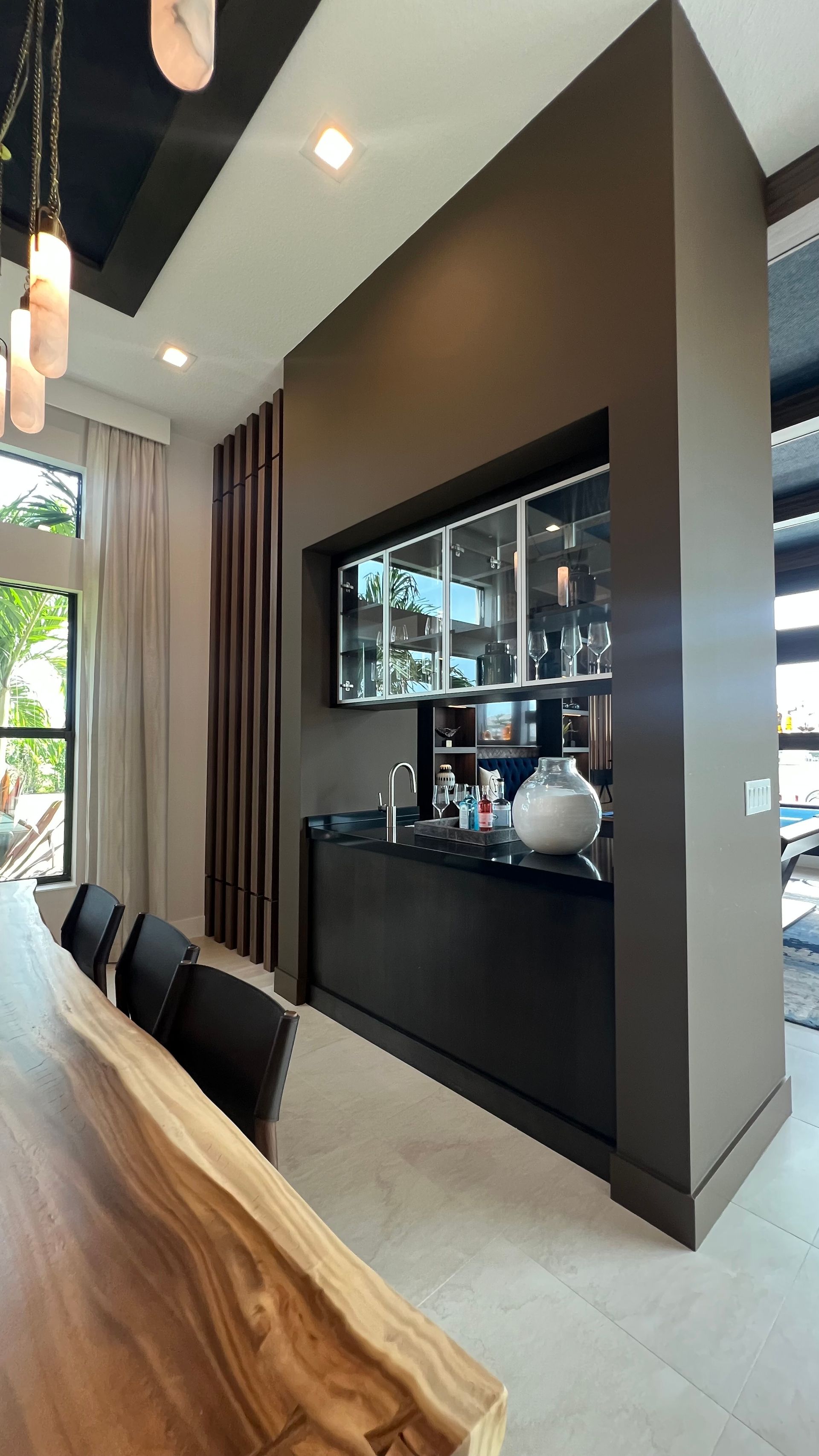 Modern home bar with black cabinets, glass upper cupboards, and a polished counter, set in a brown-walled alcove.