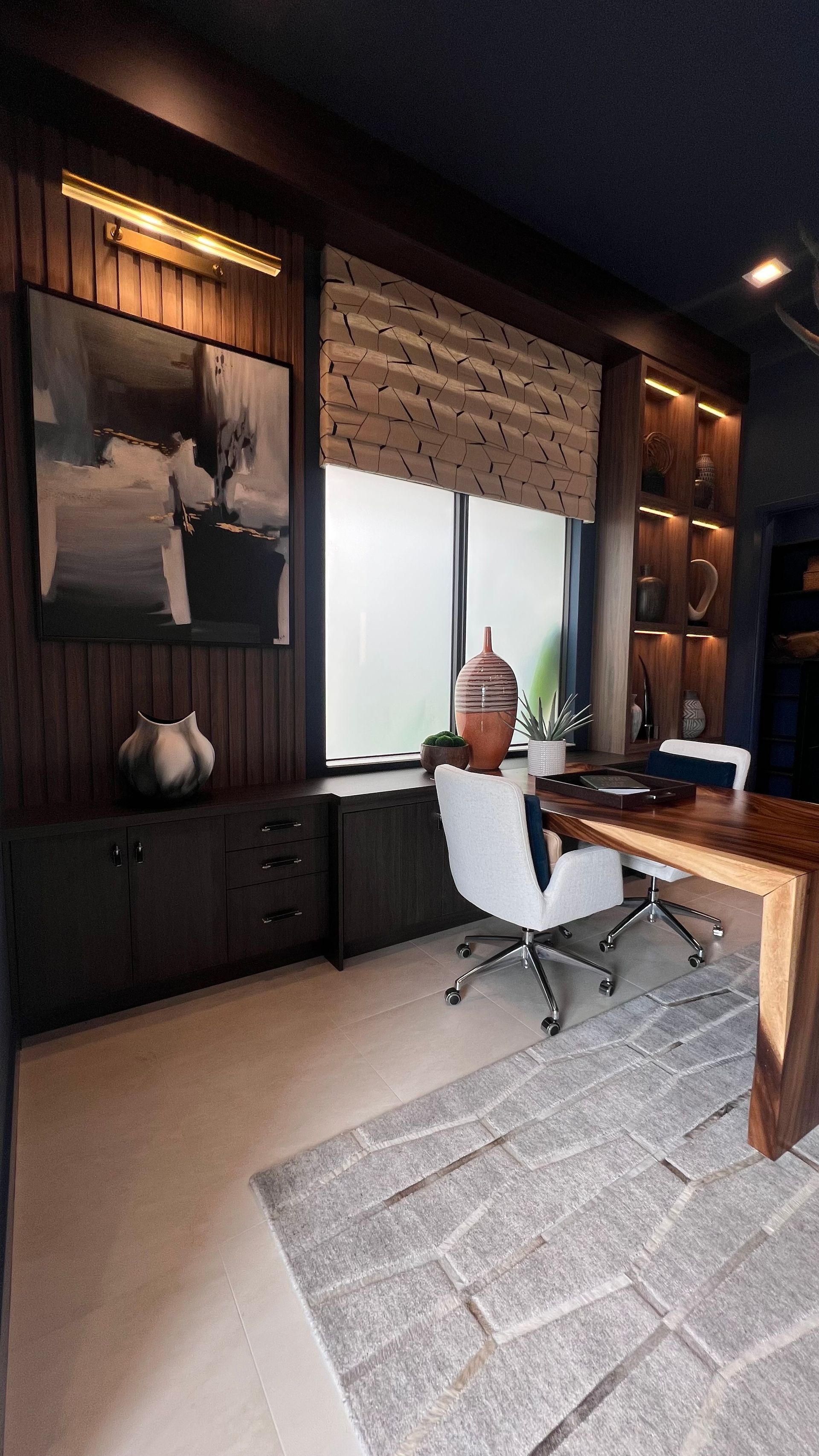 A modern home office with dark wood paneling, a wooden desk, white swivel chairs, and a geometric rug.