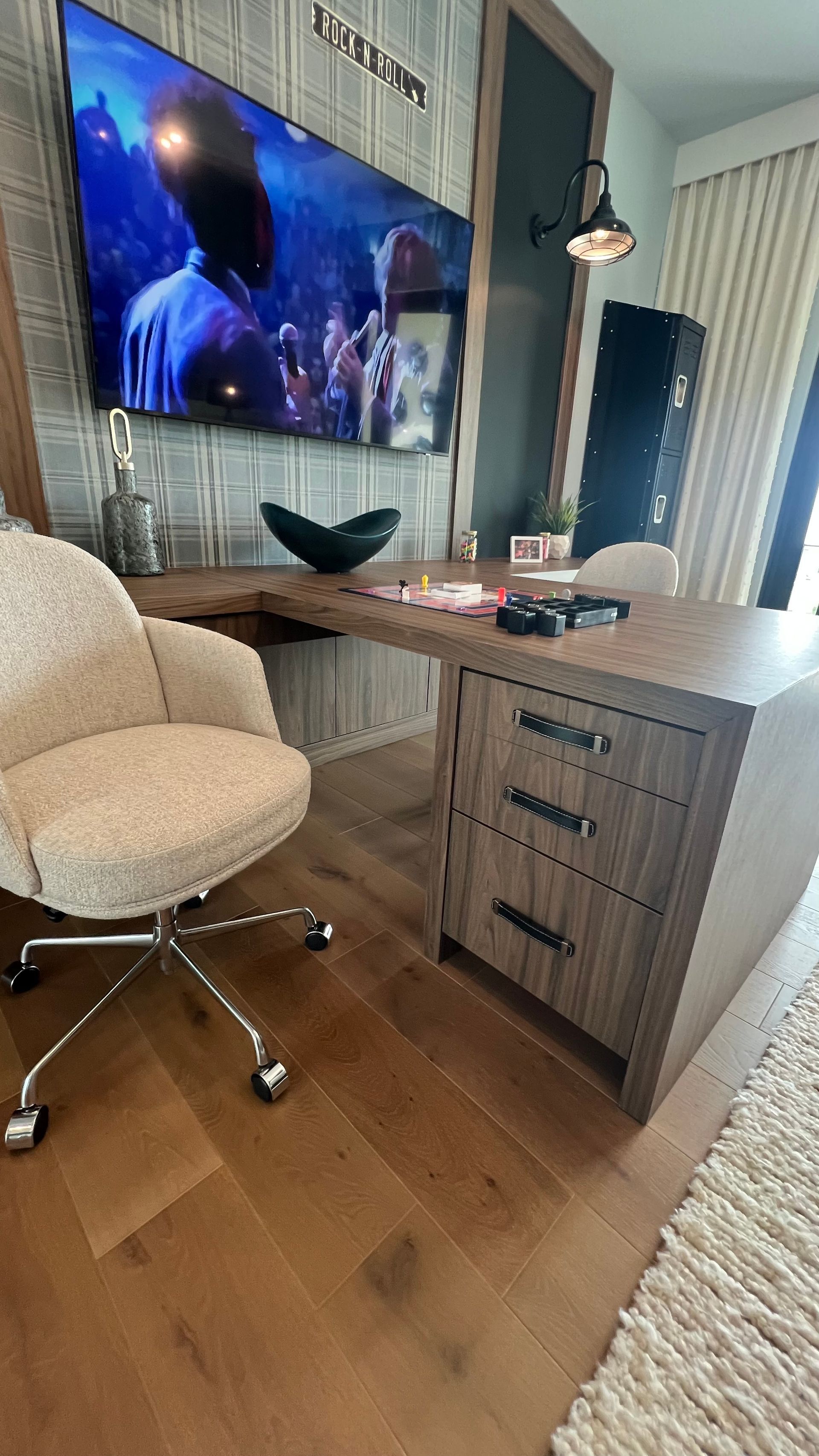 A desk with three drawers and a textured cream office chair sits beneath a wall-mounted TV in a modern room.