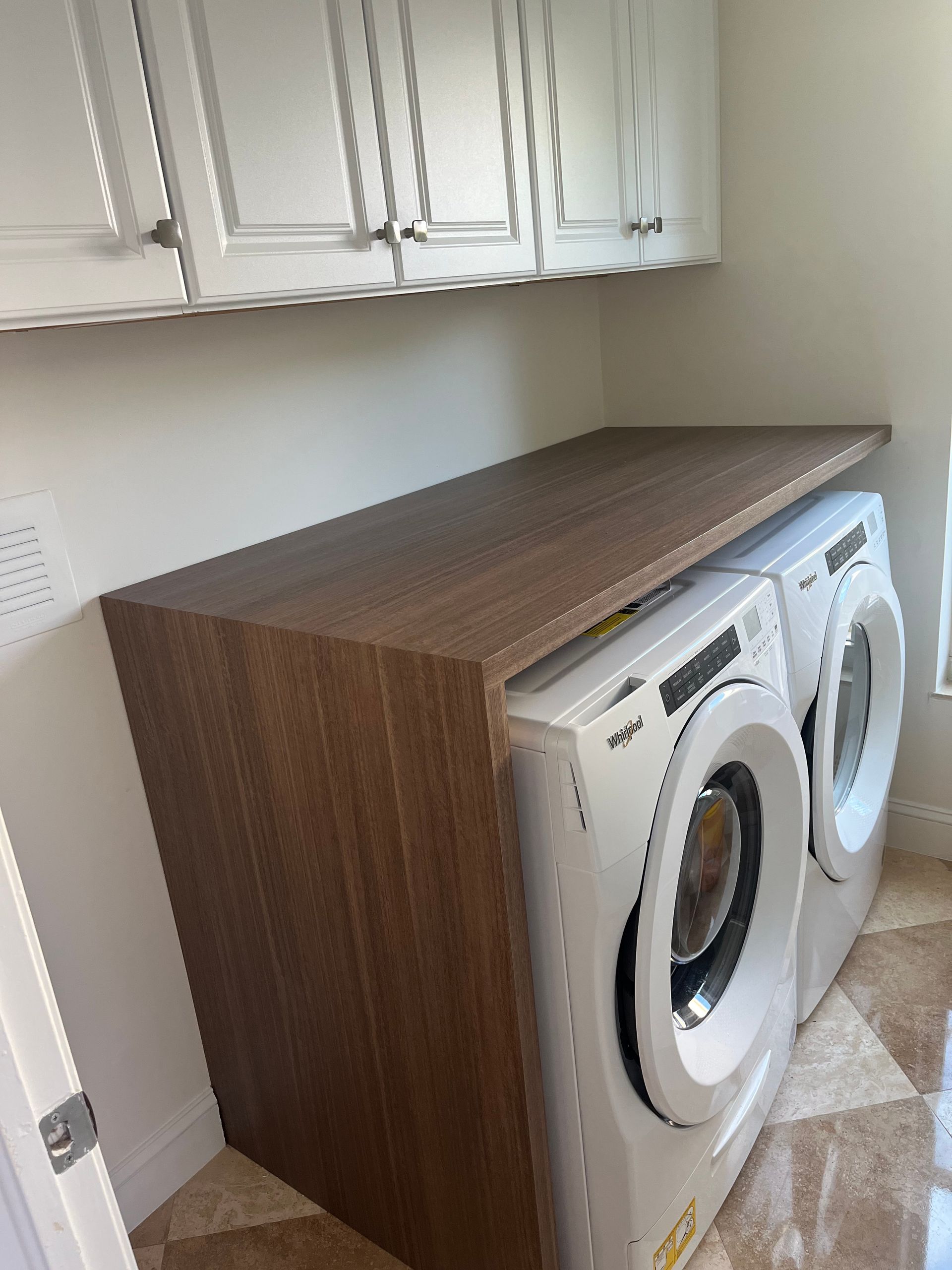 A laundry room featuring two white front-load washers under a wood-grain countertop with white wall cabinets above.