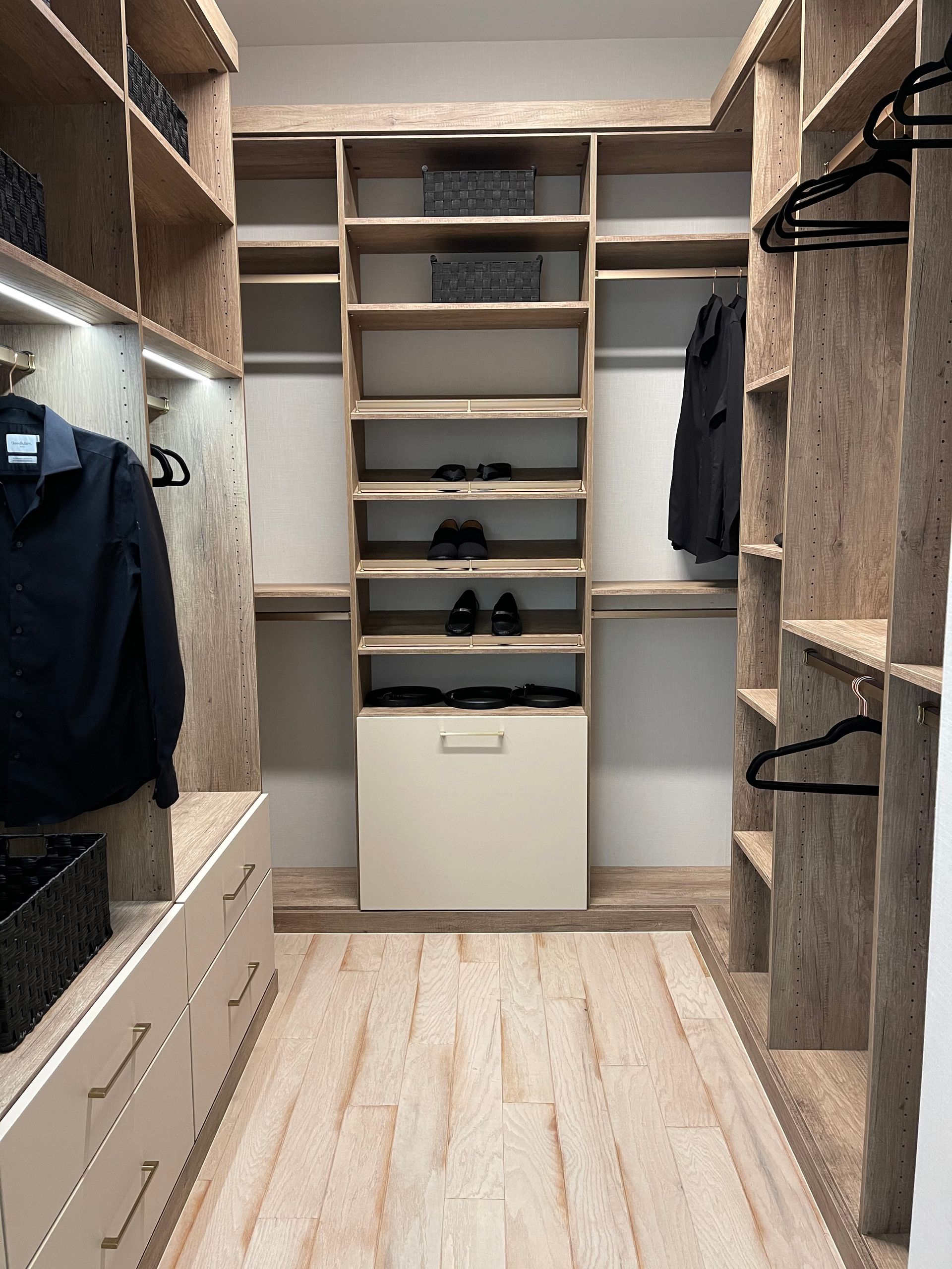 A modern walk-in closet featuring light wood shelving, hanging clothes, drawers, and a central shoe rack with carpet.