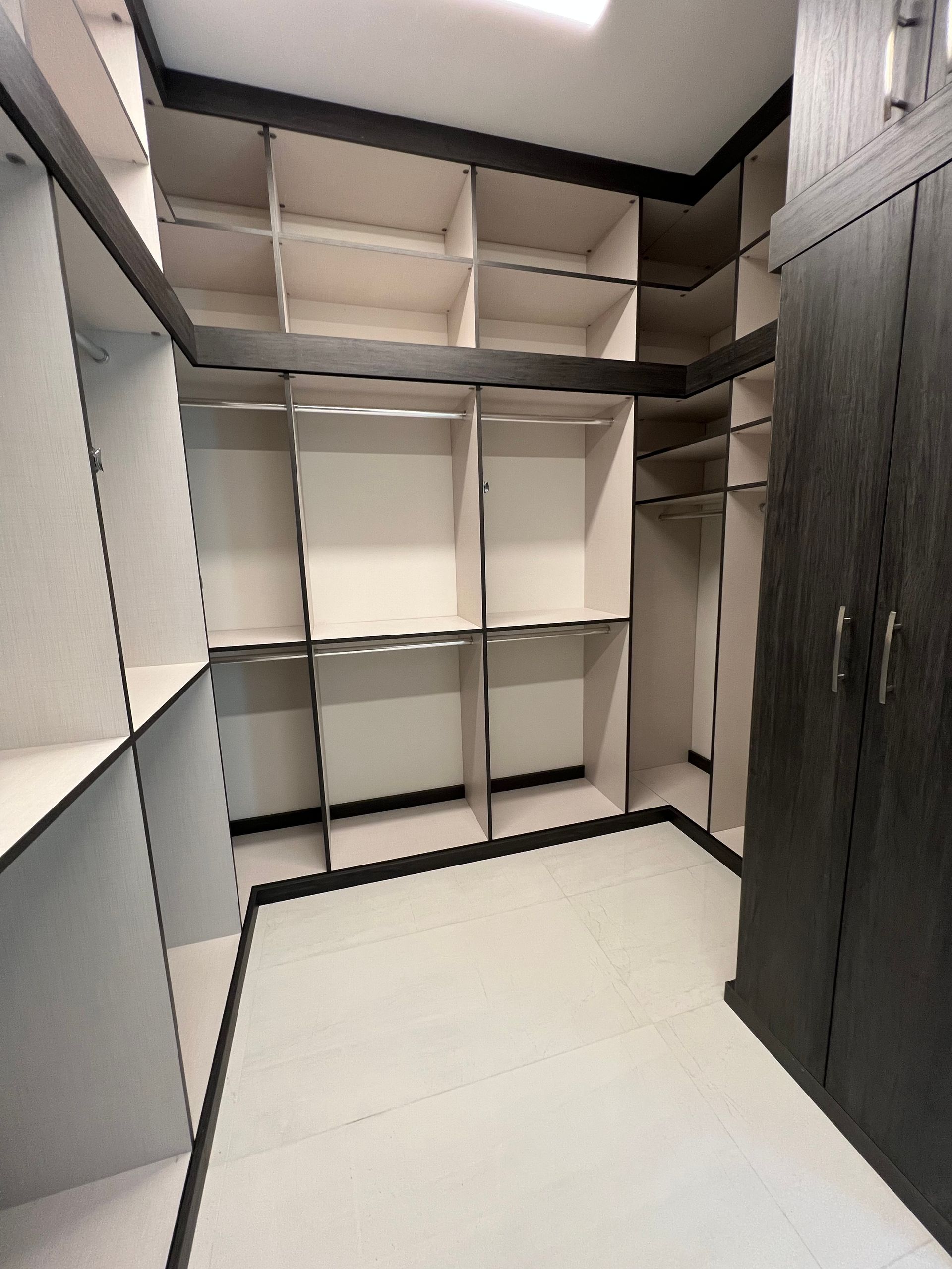 A walk-in closet featuring light-colored open shelving and hanging rods with dark-toned trim and a matching cabinet.